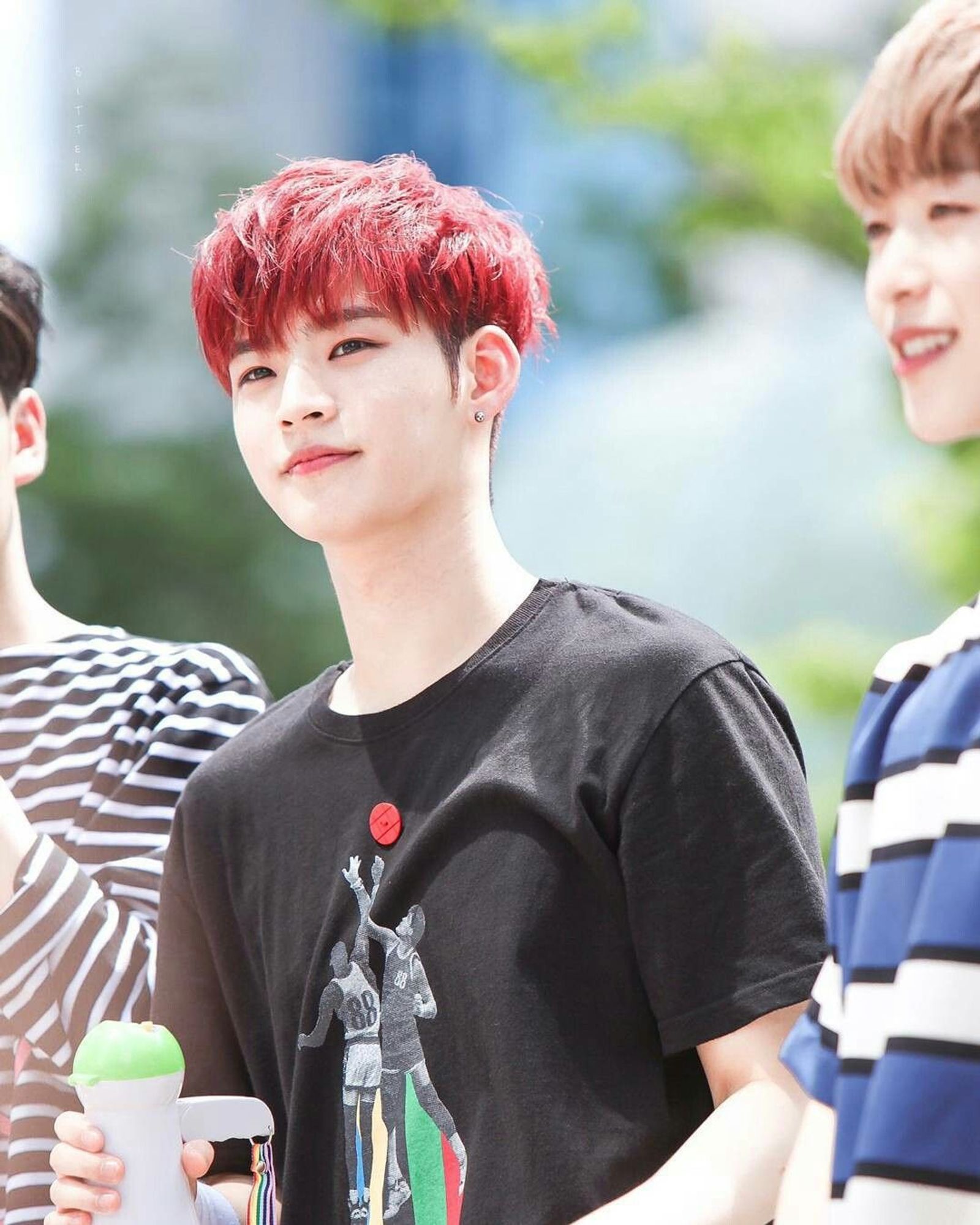 photo of Hyojin from ONF with red hair, standing next to Laun, outside with green trees in the blurred background