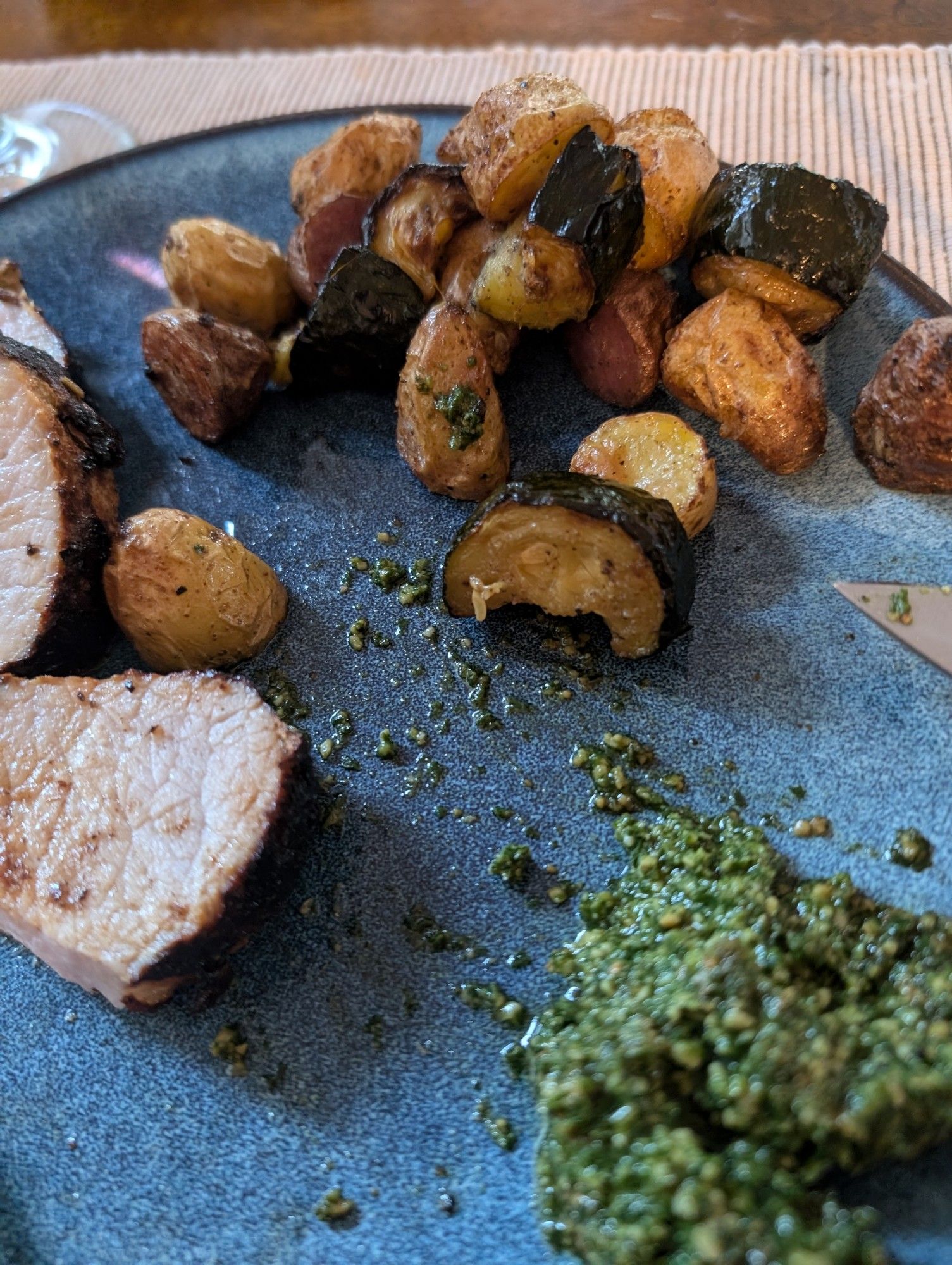 Seered pork tenderloin with roasted potatoes and zucchini with a side of pesto on a blue plate