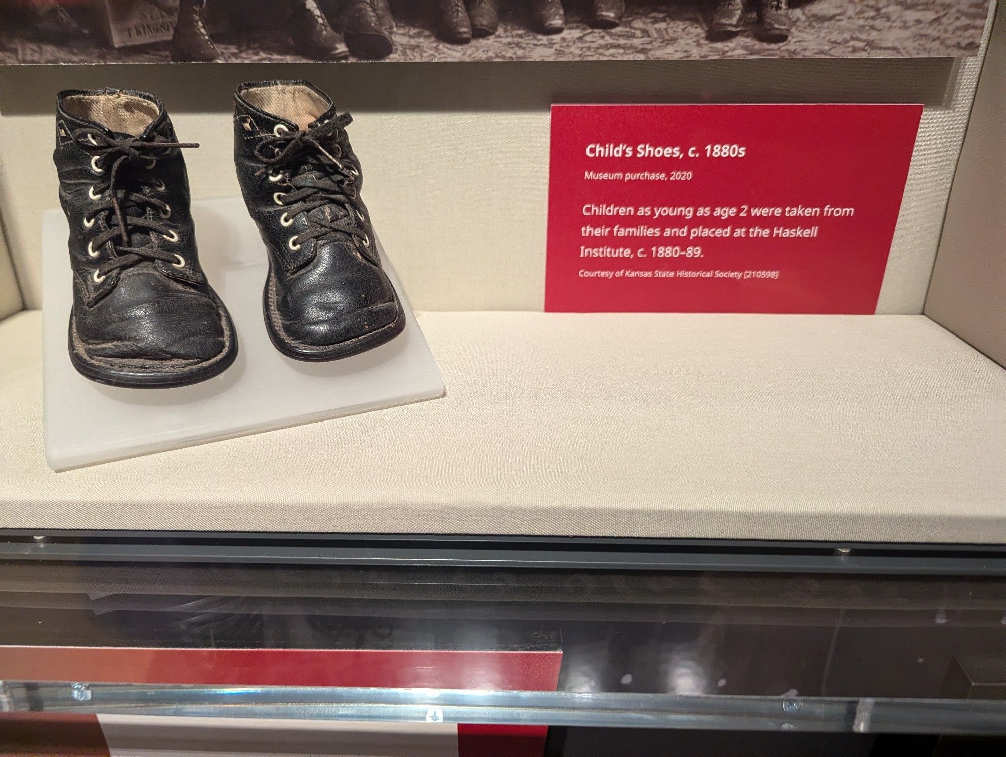 A tiny pair or worn black shoes next to a sign that reads:
Child's Shoes, c. 1880s

Museum purchase, 2020

Children as young as age 2 were taken from their families and placed at the Haskell Institute, c. 1880-89.

Courtesy of Kansas State Historical Society