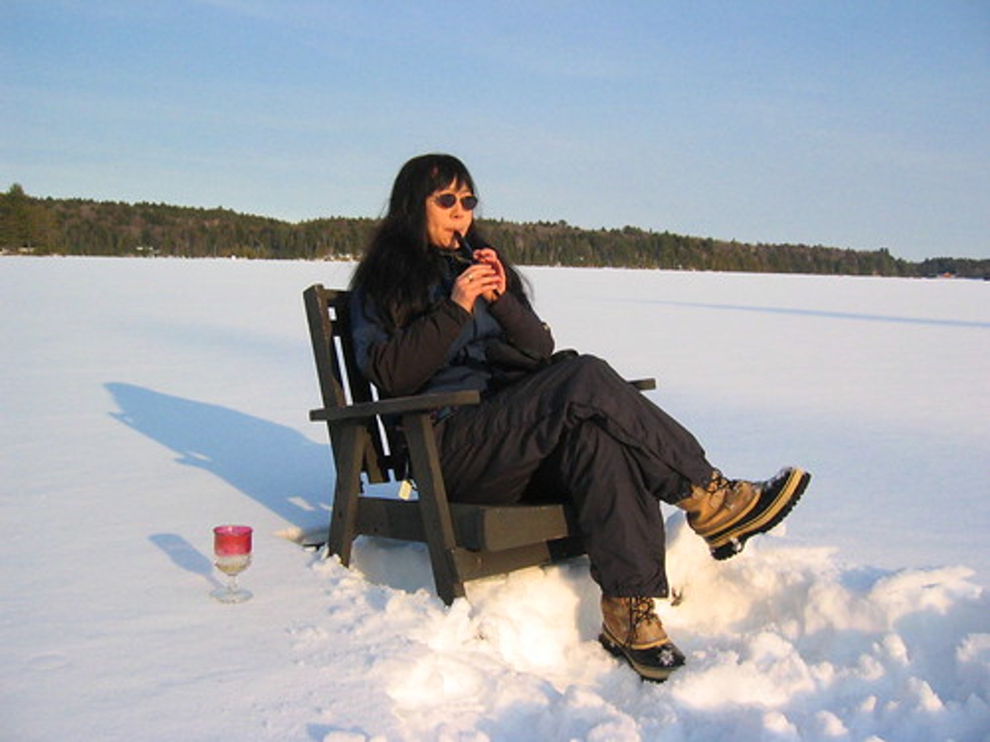 Debbie playing a tin whistle on a wooden deck chair in the middle of a frozen l ake.