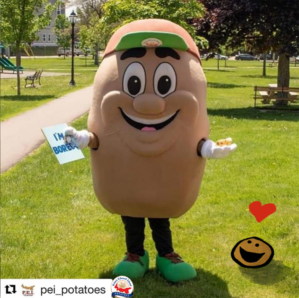 The image shows a person in a potato mascot costume standing in a park on a sunny day. The mascot is smiling widely, with large cartoonish eyes and eyebrows, wearing a green cap, green shoes, and white gloves. The mascot is holding a picture book in one hand whose title reads "I'M BORED!" in blue text, and a small Stress Potato in the other. The background includes green grass, trees, a walking path, and some park benches. In the lower right corner of the image, there is a small doodle of a smiling potato with a red heart above it. The image has logos for "PEI Potatoes" and "Prince Edward Island Potatoes" at the bottom.