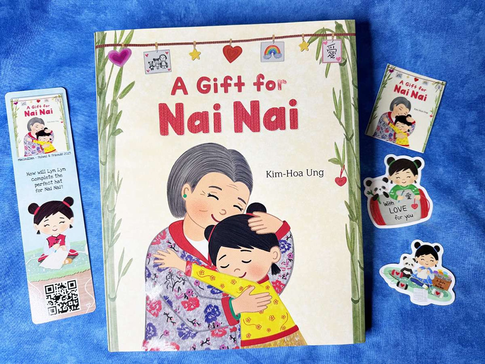 Photo of a children's book called A GIFT FOR NAI NAI by Kim-Hoa Ung on a blue background, with a bookmark and stickers. The cover shows an elderly Asian woman hugging a young Asian girl.