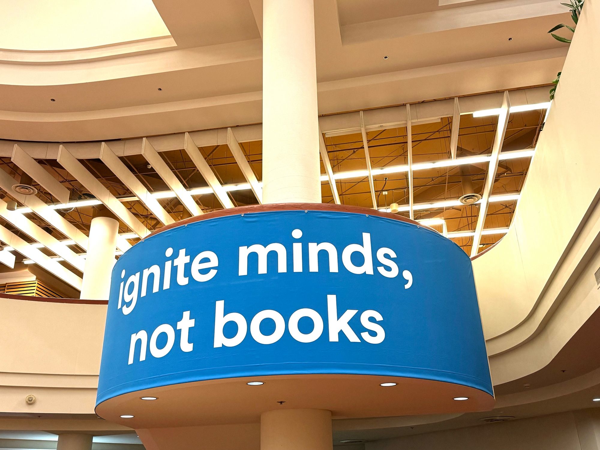 Photo of big blue sign on display against pillar. White text reads, “ignite minds, not books”