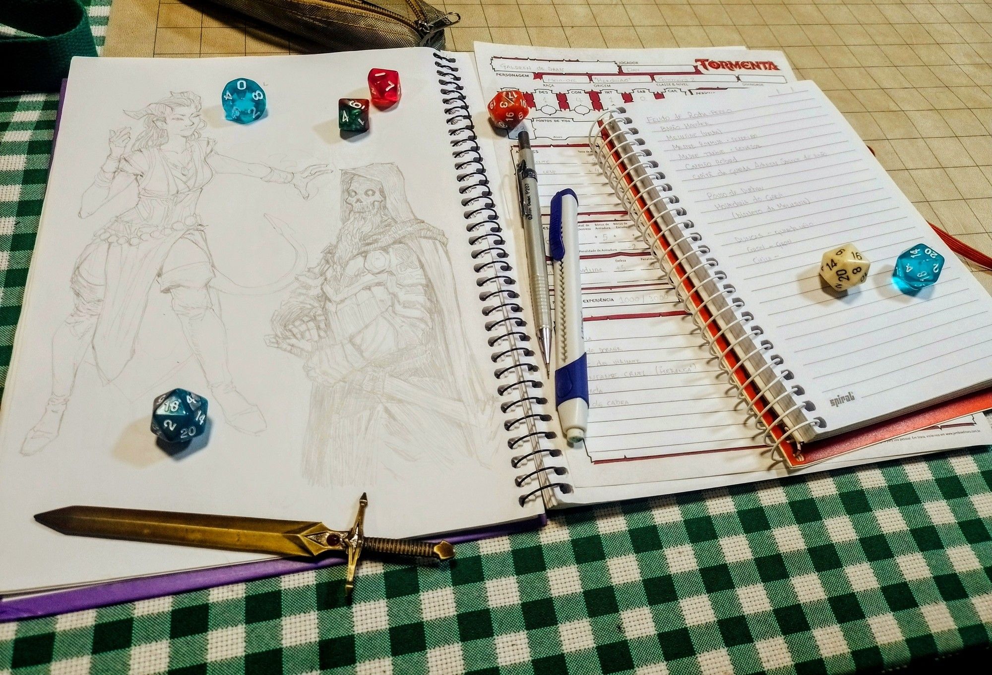 Fotografia de uma mesa com materiais de RPG de mesa (um caderno com desenhos, um com anotações, uma ficha de personagem, dados, lápis e uma espadinha em miniatura)