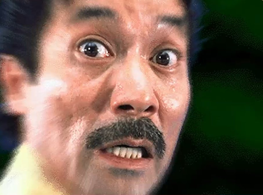 Close up image of a shocked asian man with a short trimmed mustache. The edges of the image are blurred, creating a zooming in effect to emphasize his shock.