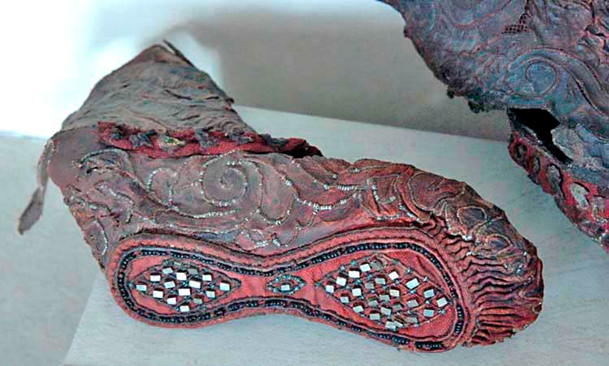 Lotus-like ornaments were sewn in the leather with sinew thread wrapped in tinfoil. The sole of the boot was decorated with glass beads, tin (or pewter), pyrite crystals and gold foil. 
H. 36 cm.