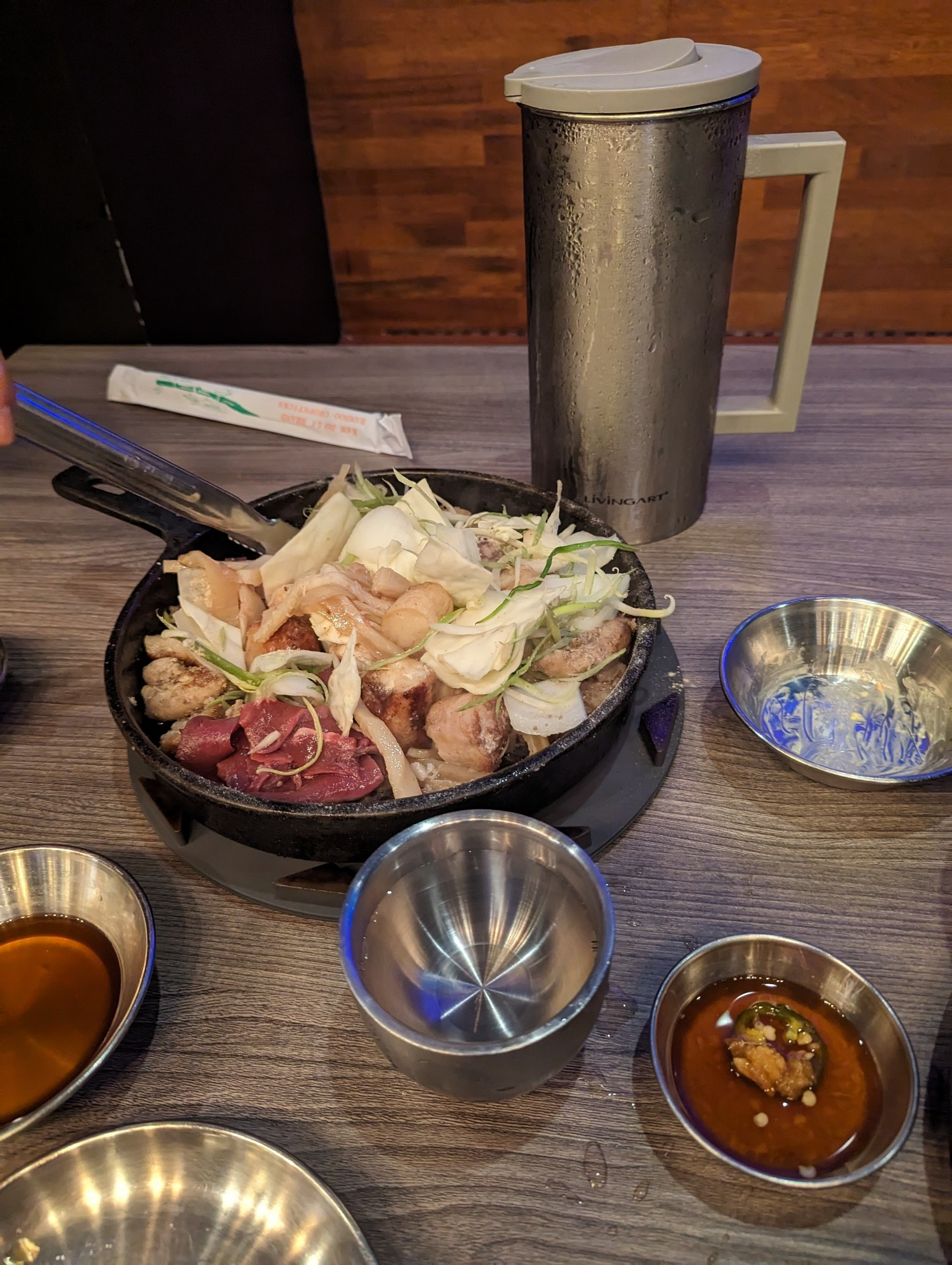 Korean BBQ beef intestines (large and small) with beef heart and vegetables sit in a large skillet with several bowls and sauces around it.