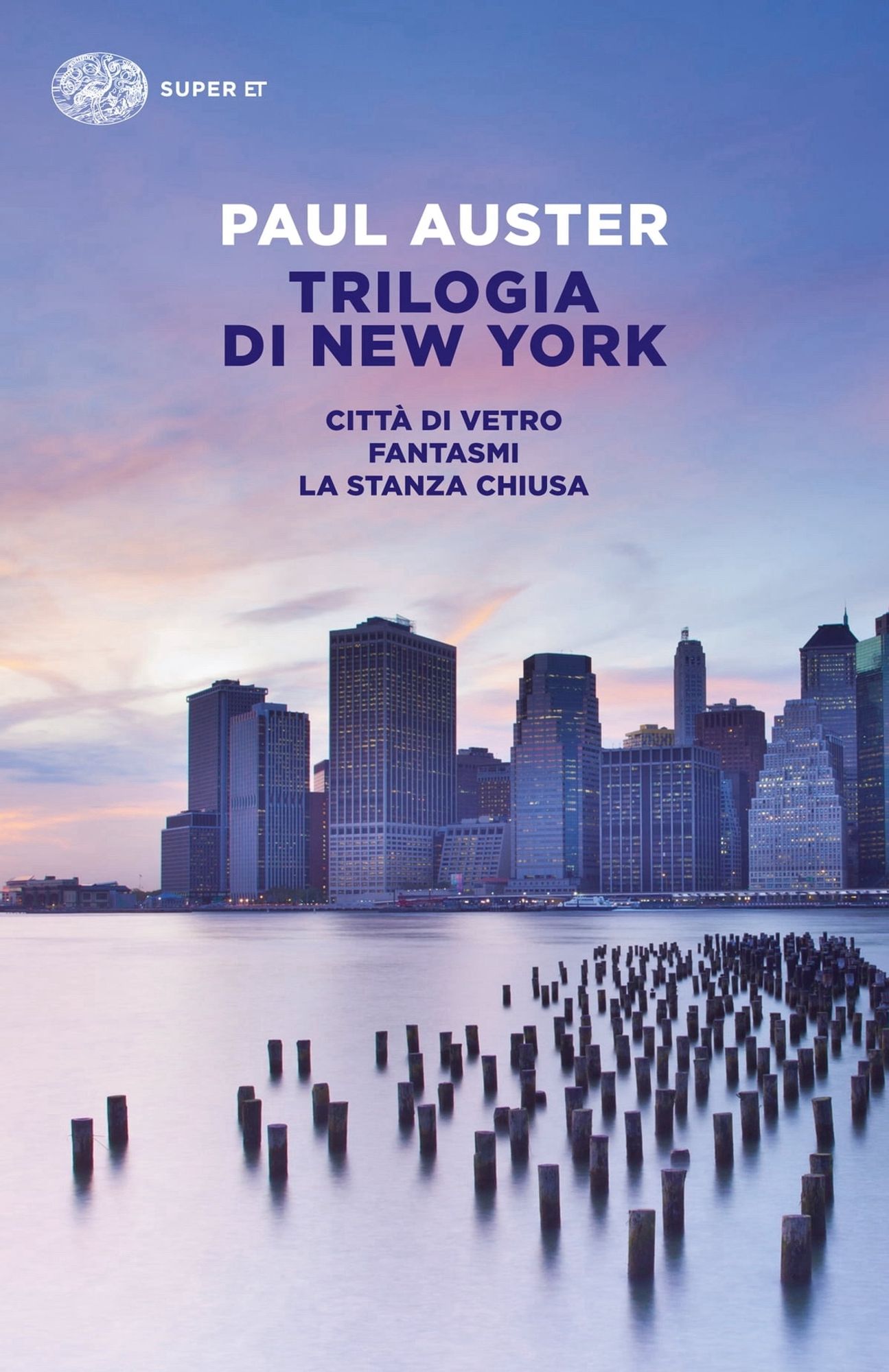 Copertina del libro Trilogia di New York dove si vede in primo piano dei piloni di legno che affiorano dall’acqua e sullo sfondo i grattacieli di Manhattan sotto un cielo azzurro con nuvole rade striate di rosa