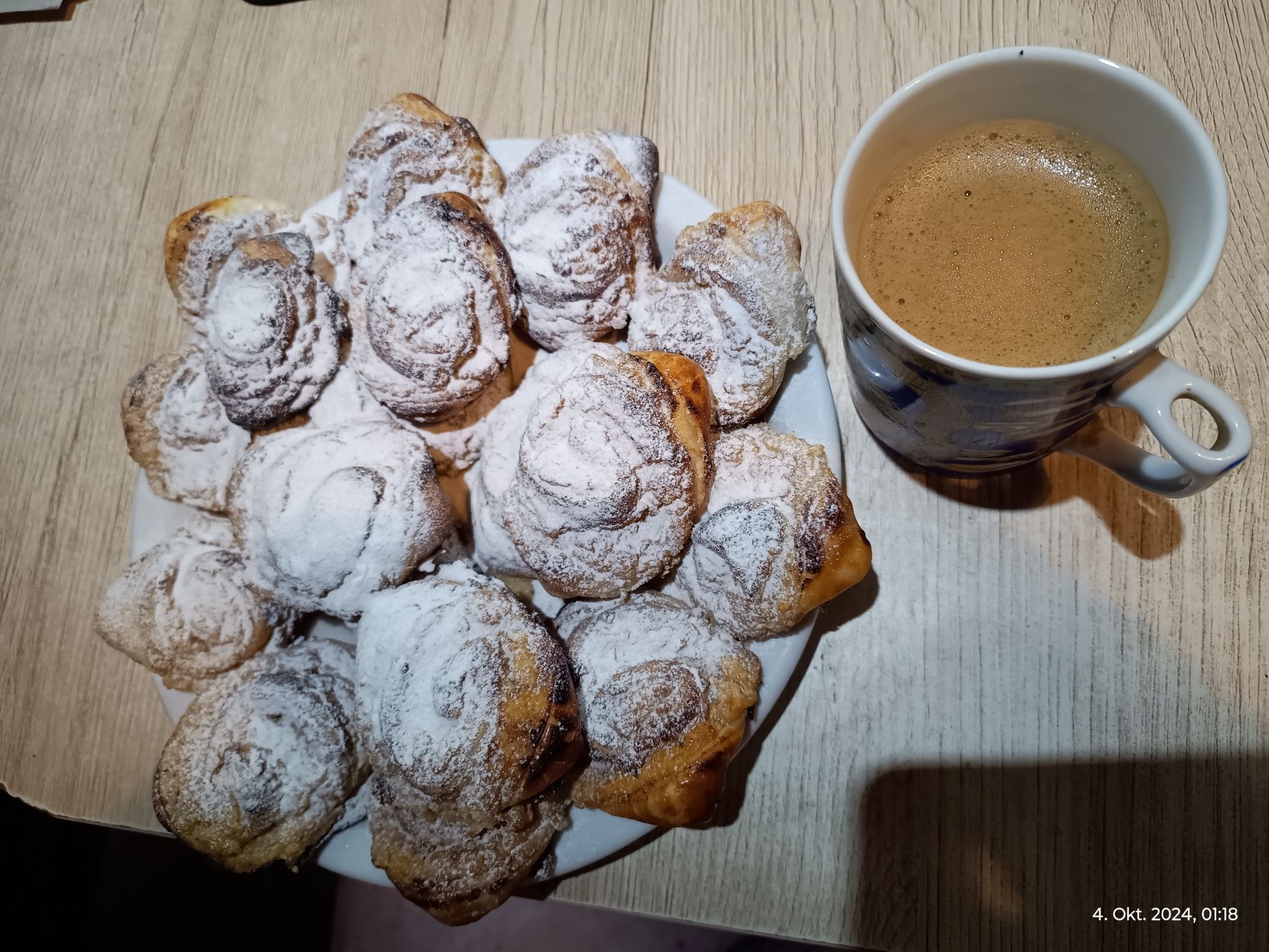 Gebackene Mini-Schnecken mit Staubzucker und rechts oben eine Tasse Cafe.