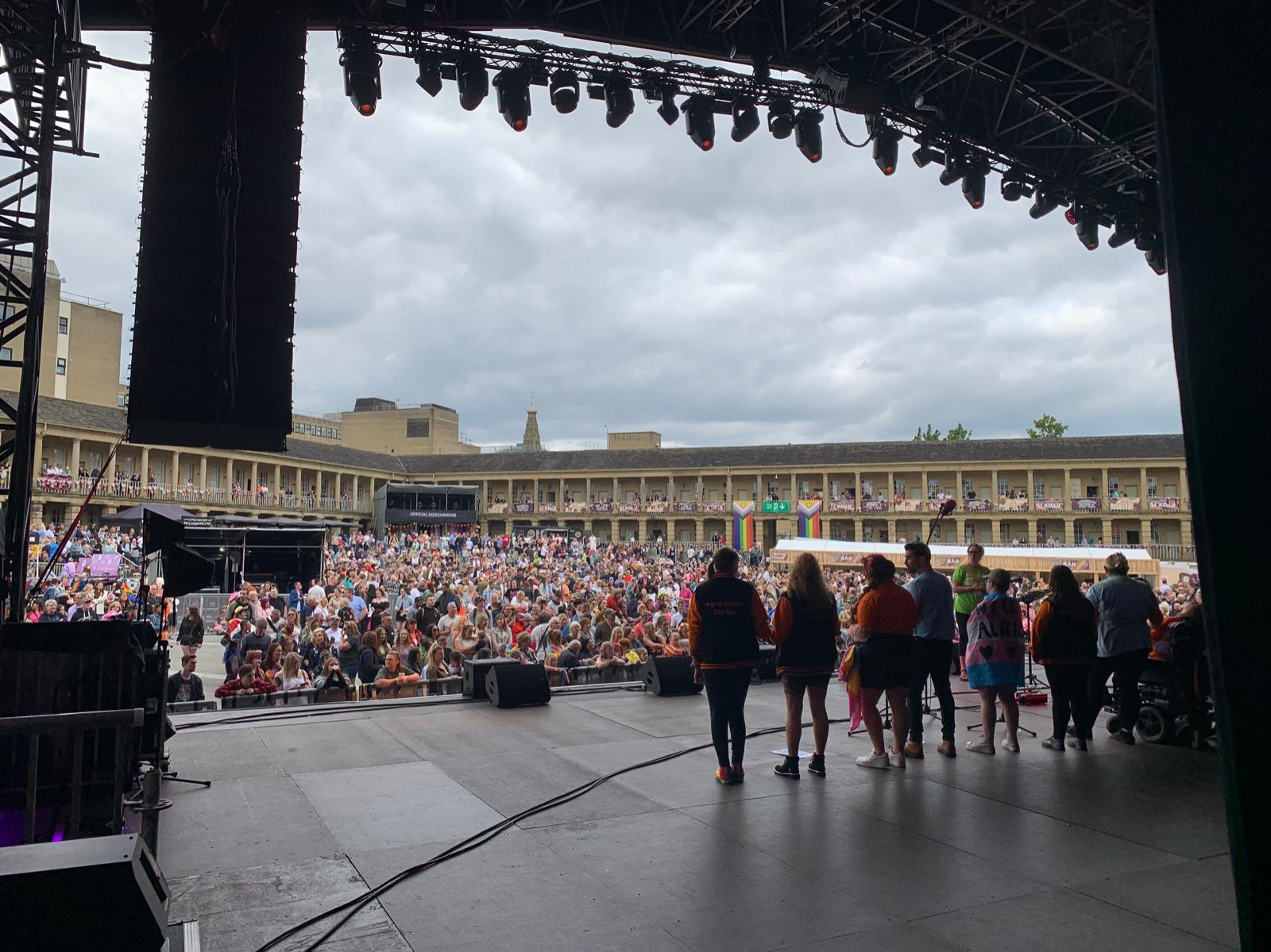 A large audience can be seen from a stage, gathered in the Piece Hall Halifax. A group of singers are silhouetted as they face the audience