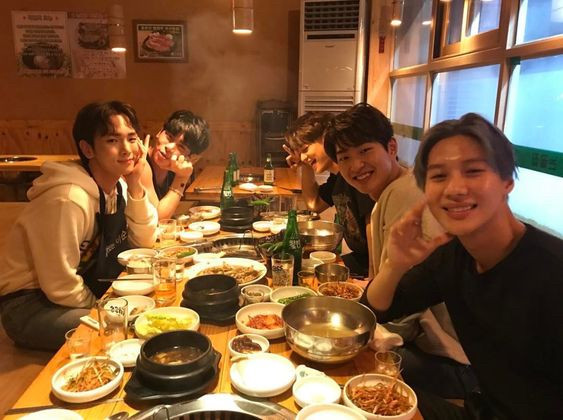 SHINee 5 sitting at a table full of food and kbbq smiling laughing and happy drunk together 