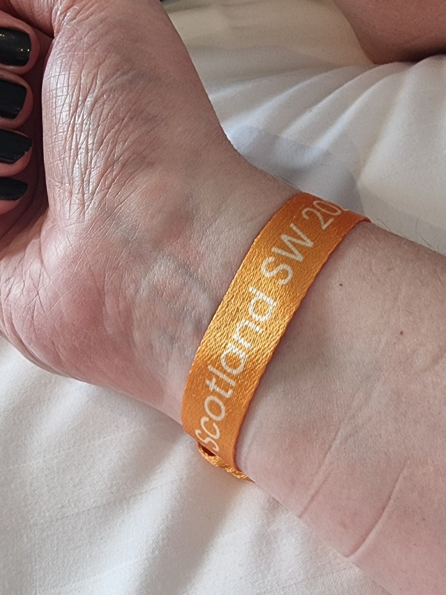 My arm with an orange wristband saying *redacted* Scotland SW 2024