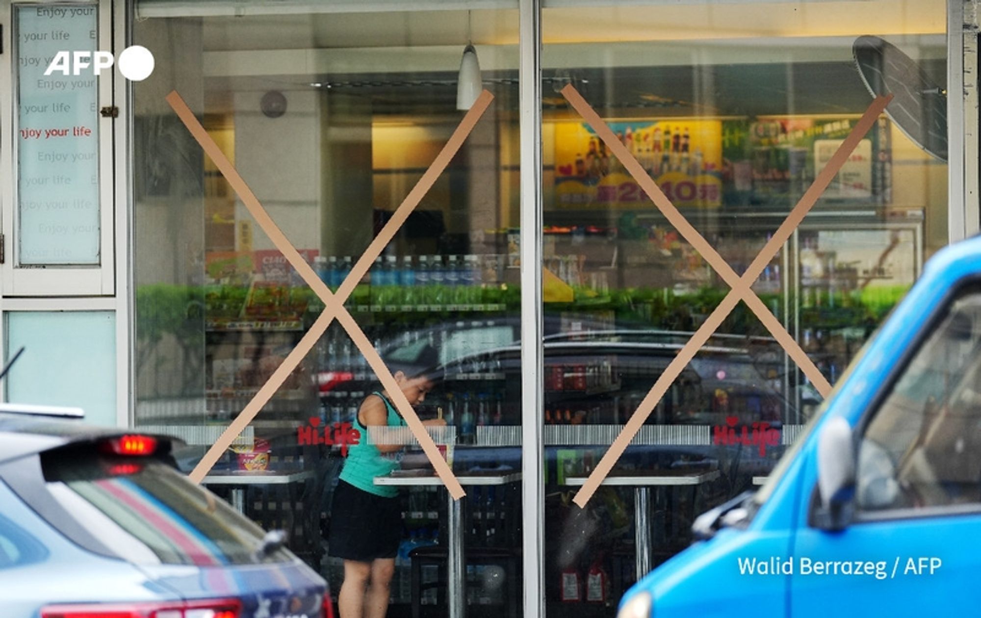 A scene depicting a convenience store in Taiwan with its glass entrance door covered by large, cross-shaped strips of brown tape, indicating that it is closed due to Typhoon Krathon. Inside the store, a person in a black skirt and a teal top can be seen, seemingly preparing to leave or possibly purchasing items before the storm. The store’s shelves are visible through the glass, stocked with various products. Outside the store, a blue vehicle is parked, partially visible at the right edge of the image. The overall atmosphere conveys a sense of caution and preparedness in response to the impending typhoon, with the weather appearing overcast.