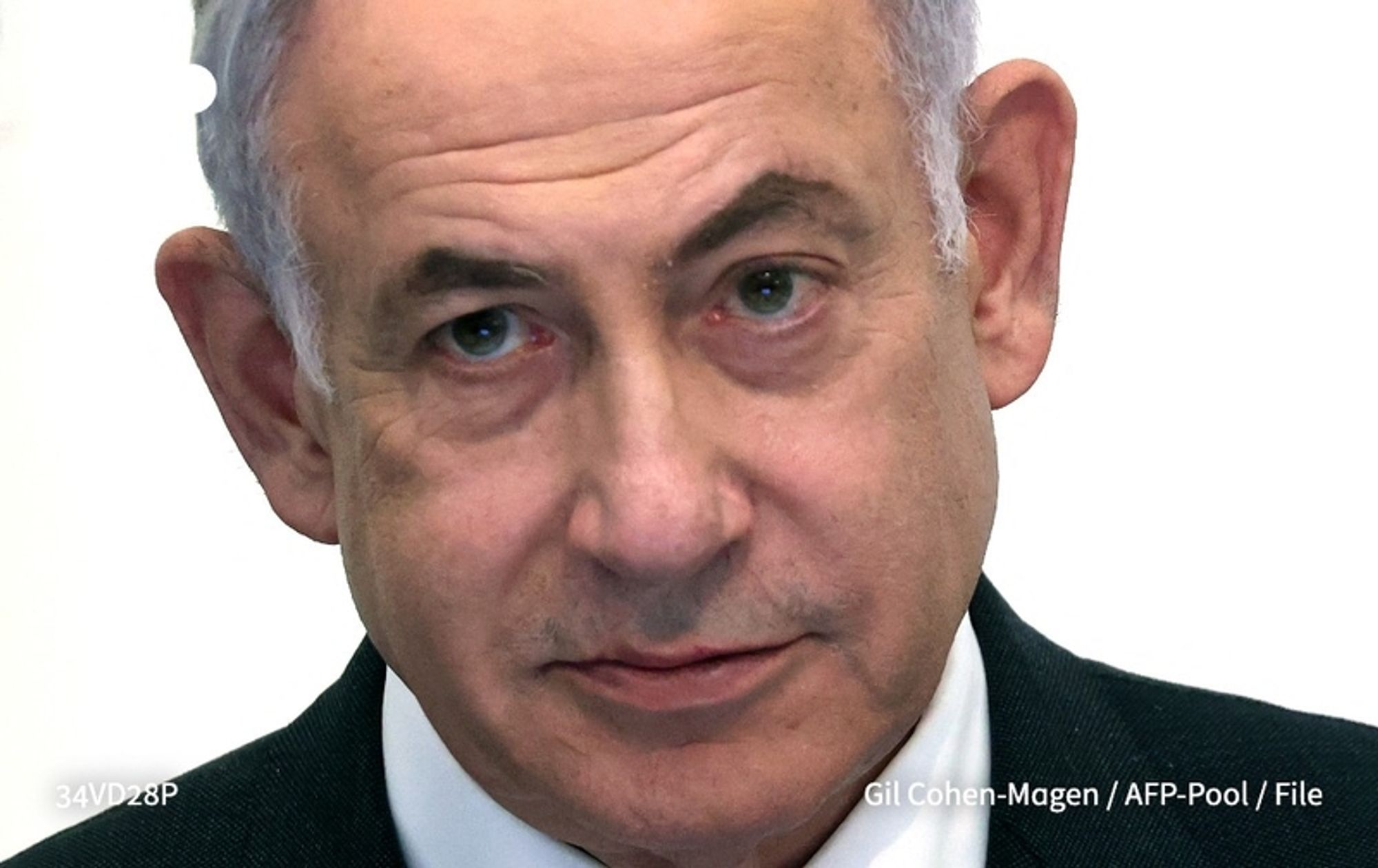 A close-up image of Benjamin Netanyahu, the Prime Minister of Israel. He is facing slightly to the left, with a serious expression on his face. Netanyahu has short, light-colored hair that shows signs of graying at the temples. His ears are somewhat protruding, and he has a faint reflection in his green eyes, which display a focused gaze. He is wearing a dark suit with a light-colored shirt underneath, and a subtle gray tie. The background is a soft, neutral tone that doesn't distract from his figure. This image reflects the gravity of his statements about changing the security landscape in the region following attacks on October 7.