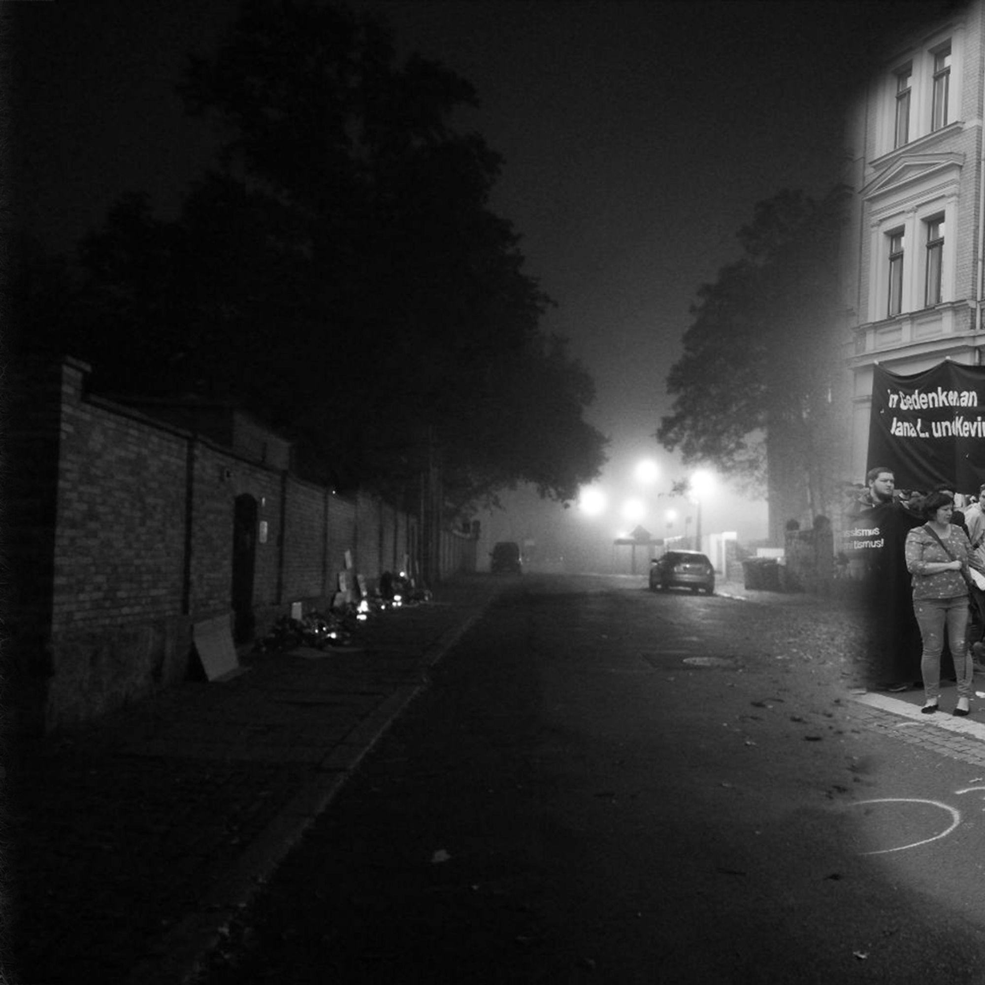 Ein schwarz-weiß-Bild: Die Synagoge von Halle nach dem antisemitischen, rassistischen und misogynen Anschlag von Halle und Wiedersdorf. Das Foto zeigt den Blick die Straße hinunter, an der Mauer der Synagoge links im Bild wurden Kerzen und Blumen abgelegt.