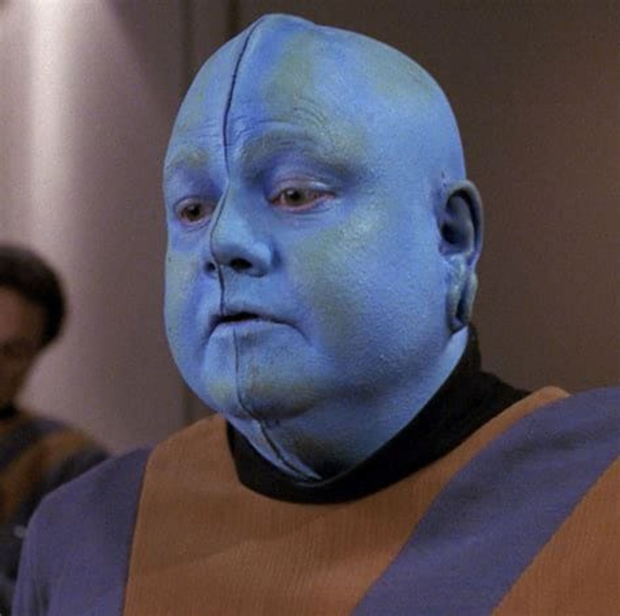 Mot from Star Trek: The Next Generation. A bald, male Bolian wearing a blue and orange patterned jumper.