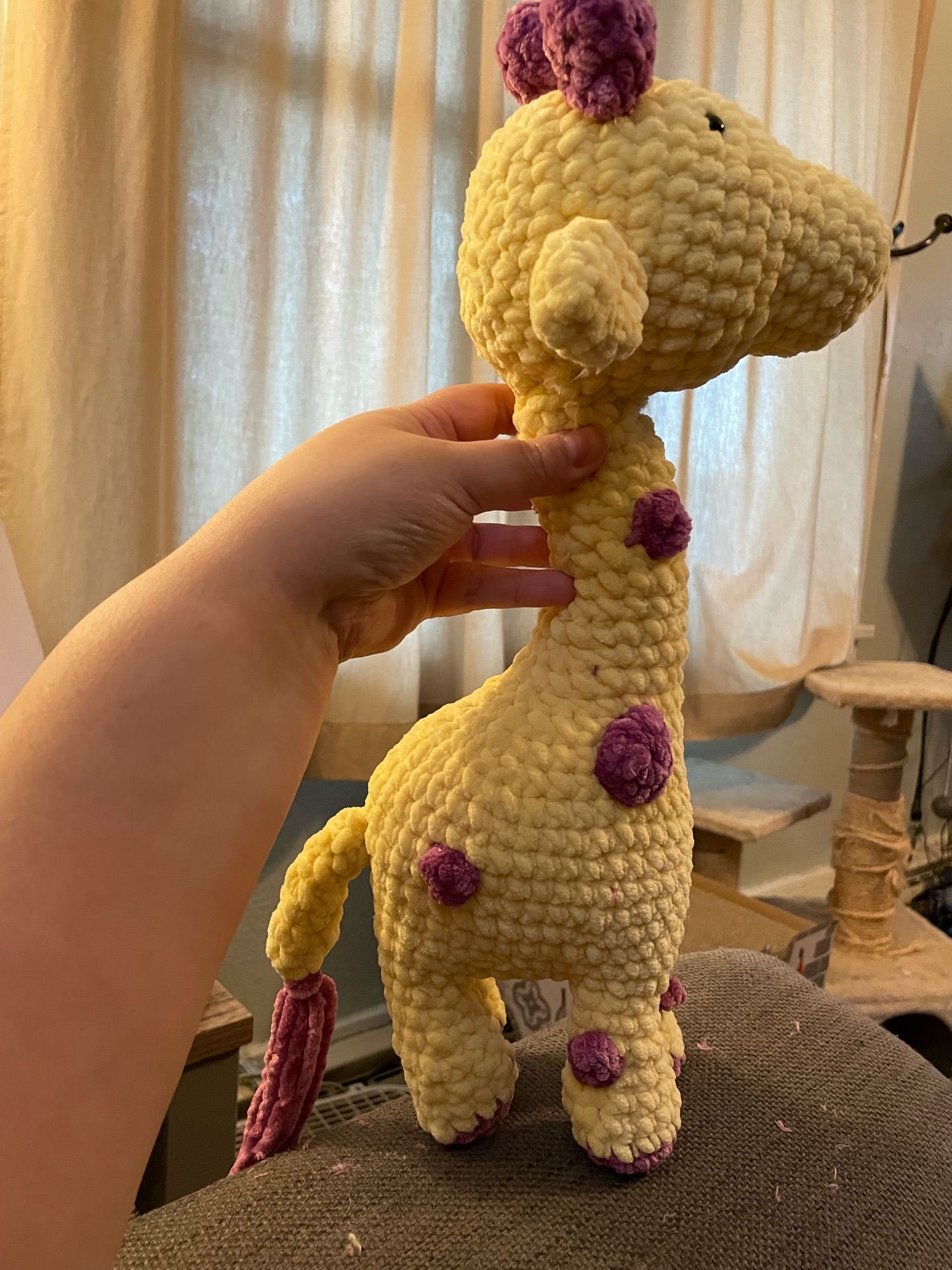 A yellow crochet giraffe with purple spots, horns, and tail tuft