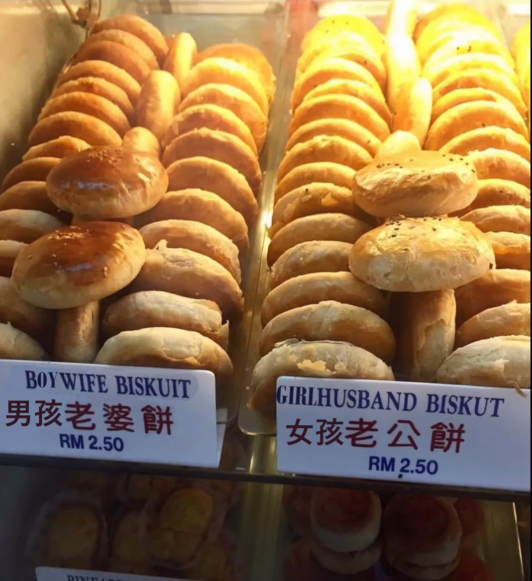 in the warm glow of a Chinese bakery's display shelves, a hastily photoshopped set of shelves reading in English and Chinese "Boywife Biskuit" and a "Girlhusband biskut" next to each other. Both of them look like very similar golden brown flaky pastries and cost only RM 2.50.