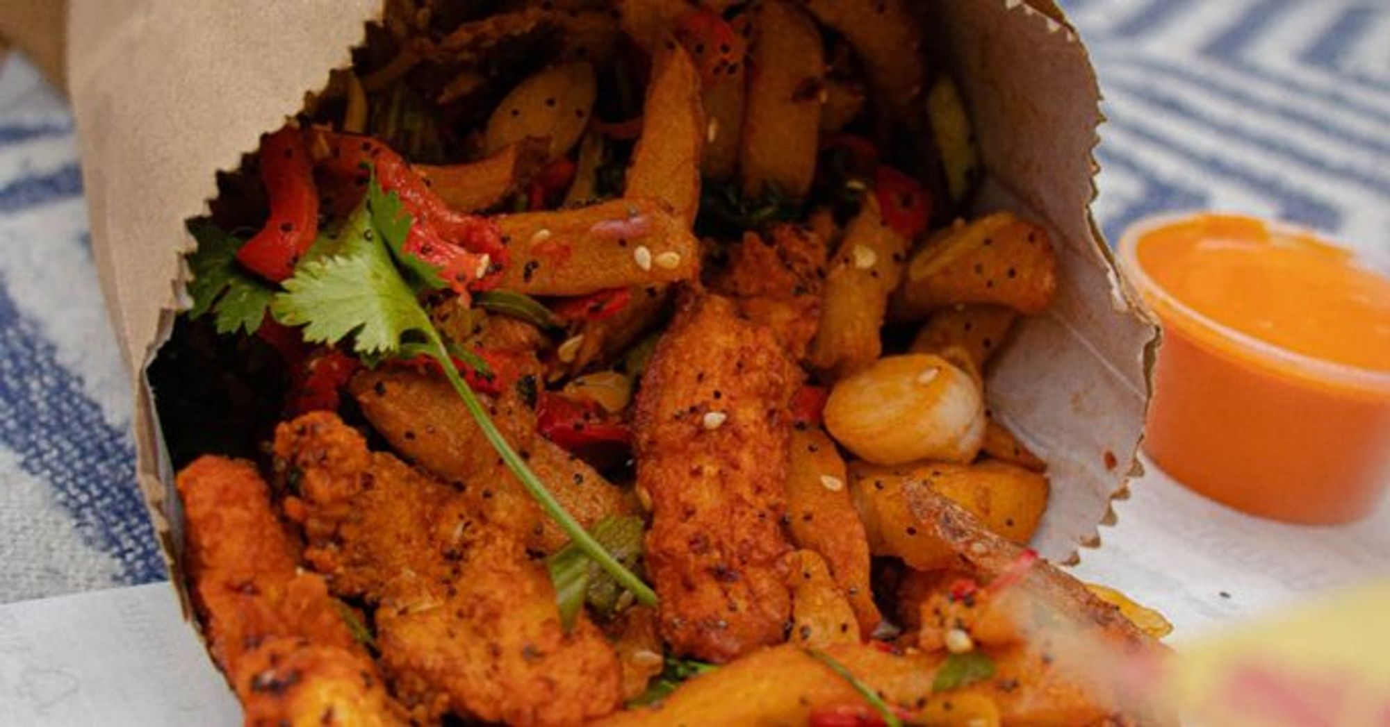 A photo of said Spice bag in a paper bag with tiny fried chicken bites covered in spices with potato fries and red peppers with neon orange curry sauce on the side.