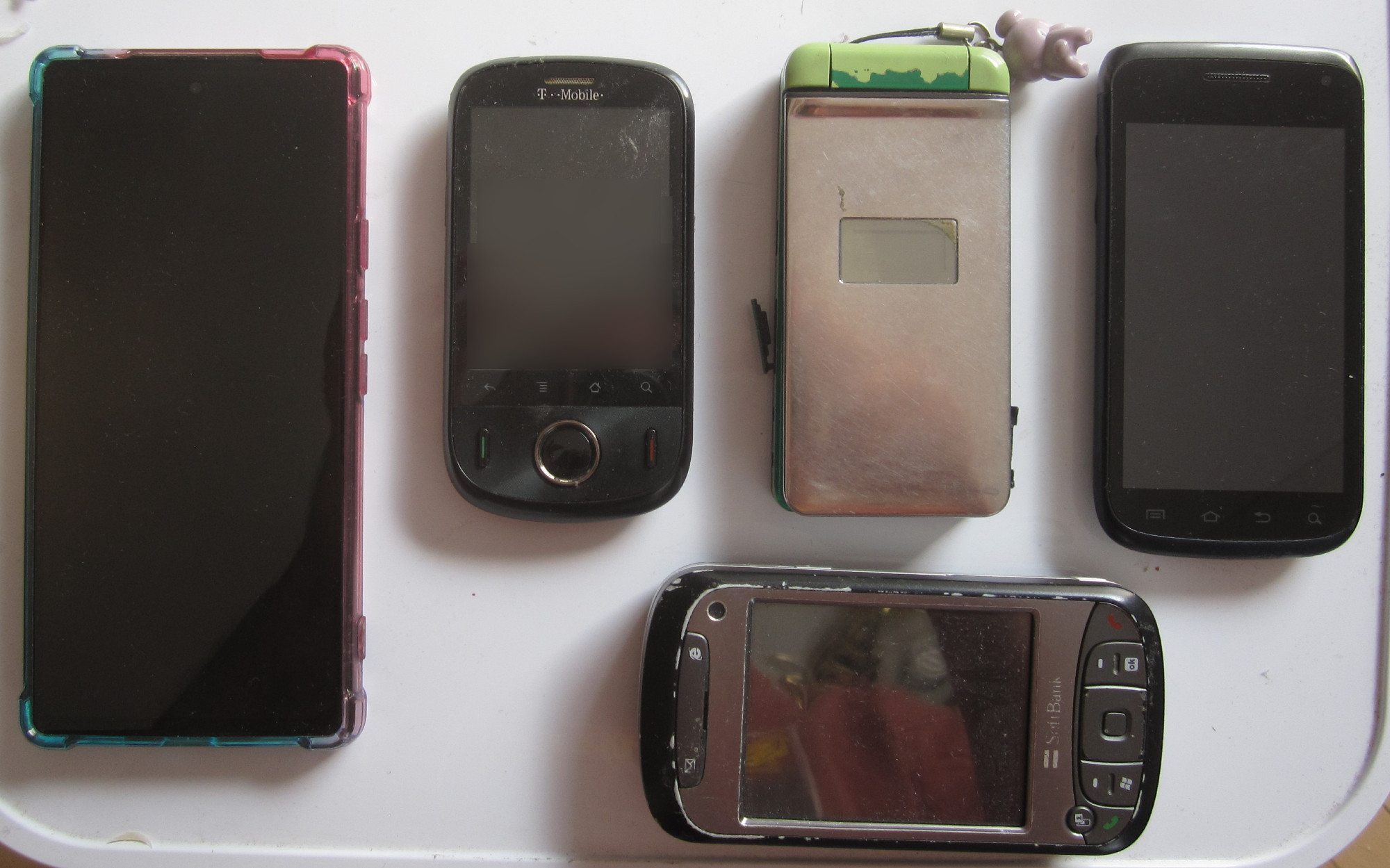 a pixel 6a dwarfing older, smaller cellphones: a huawei ideos, a Softbank 912T, a Samsung SGH-T679, and a Softbank X01HT (aka HTC Hermes 200); the 6a is probably twice as big, by area, as the other phones