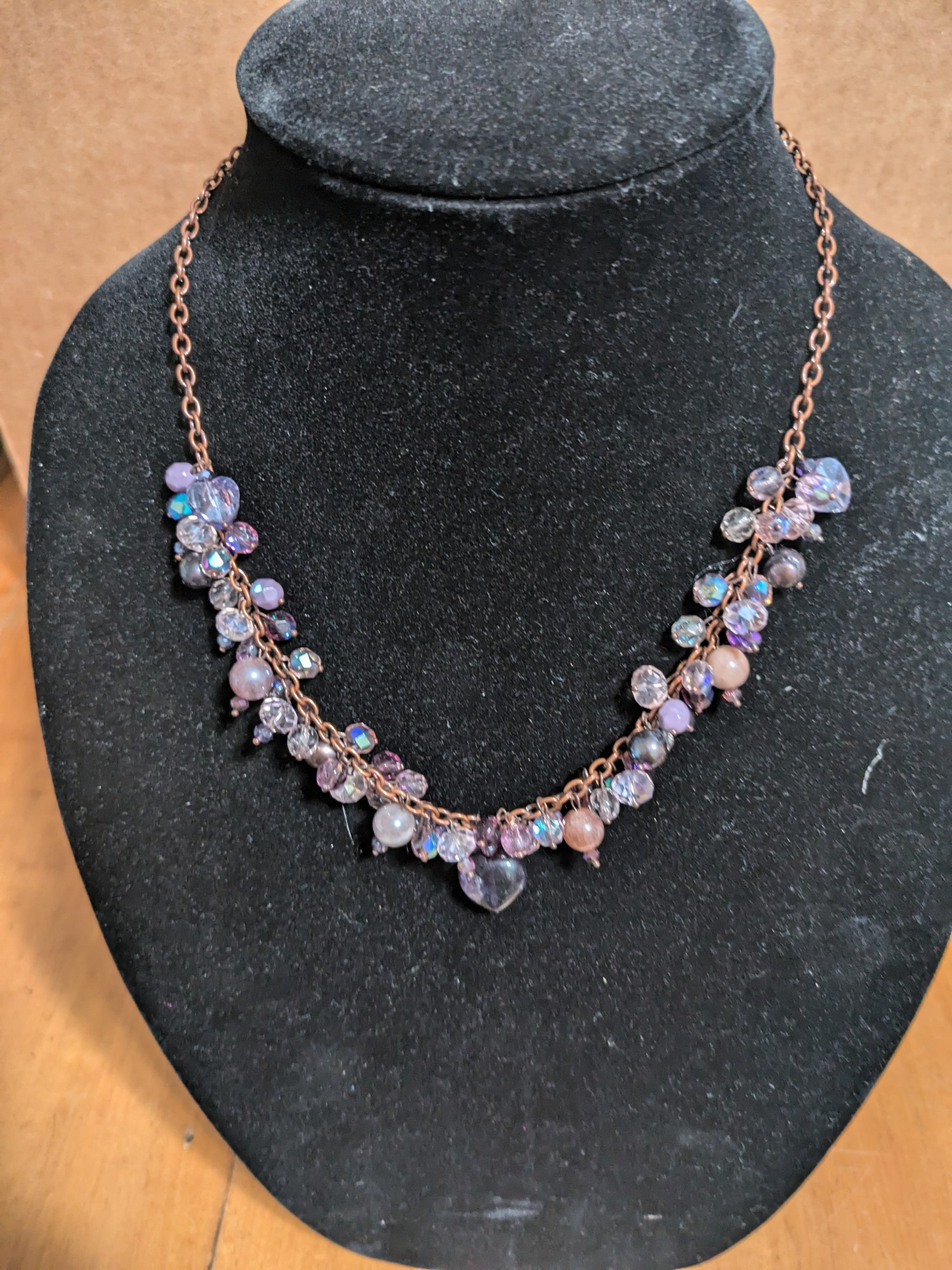 Beaded necklace on antique copper chain. Beads are a mix of amethyst and fluorite hearts, sunstone spheres, natural pearls, and faceted glass. Colors range from a purplish tan to pinks, lavenders, and purples. 