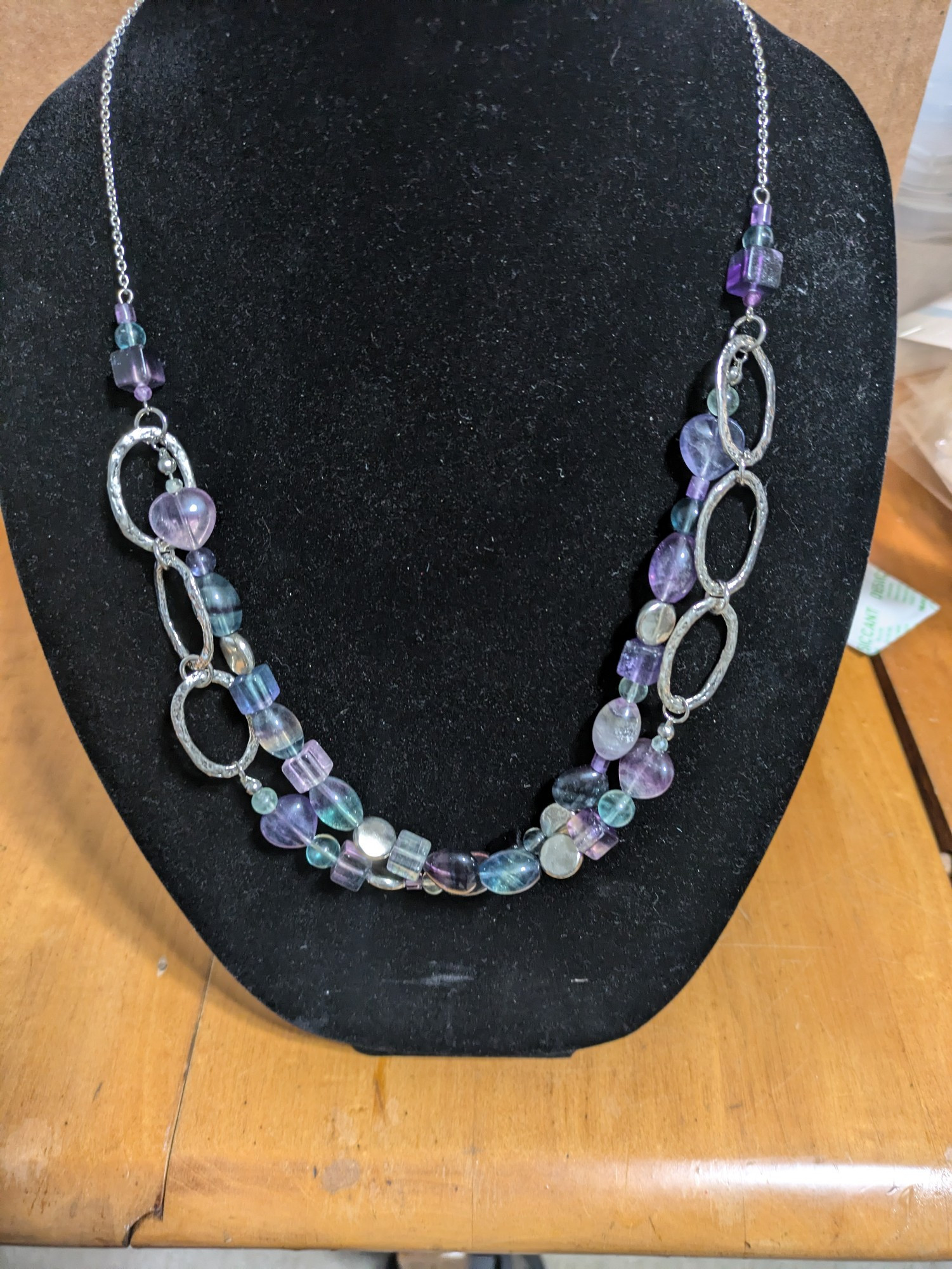 Double stranded beaded necklace in the purples and bluish greens of fluorite. The beads are hearts, ovals, squares, and spheres. It has silver squarish accent beads and hammered silver ovals. 