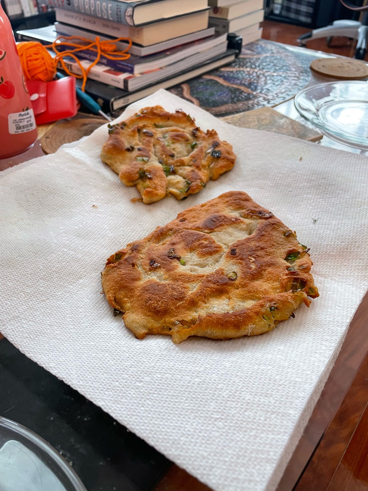 Two thick scallion pancakes sit on a paper towel. The pancakes are golden brown.