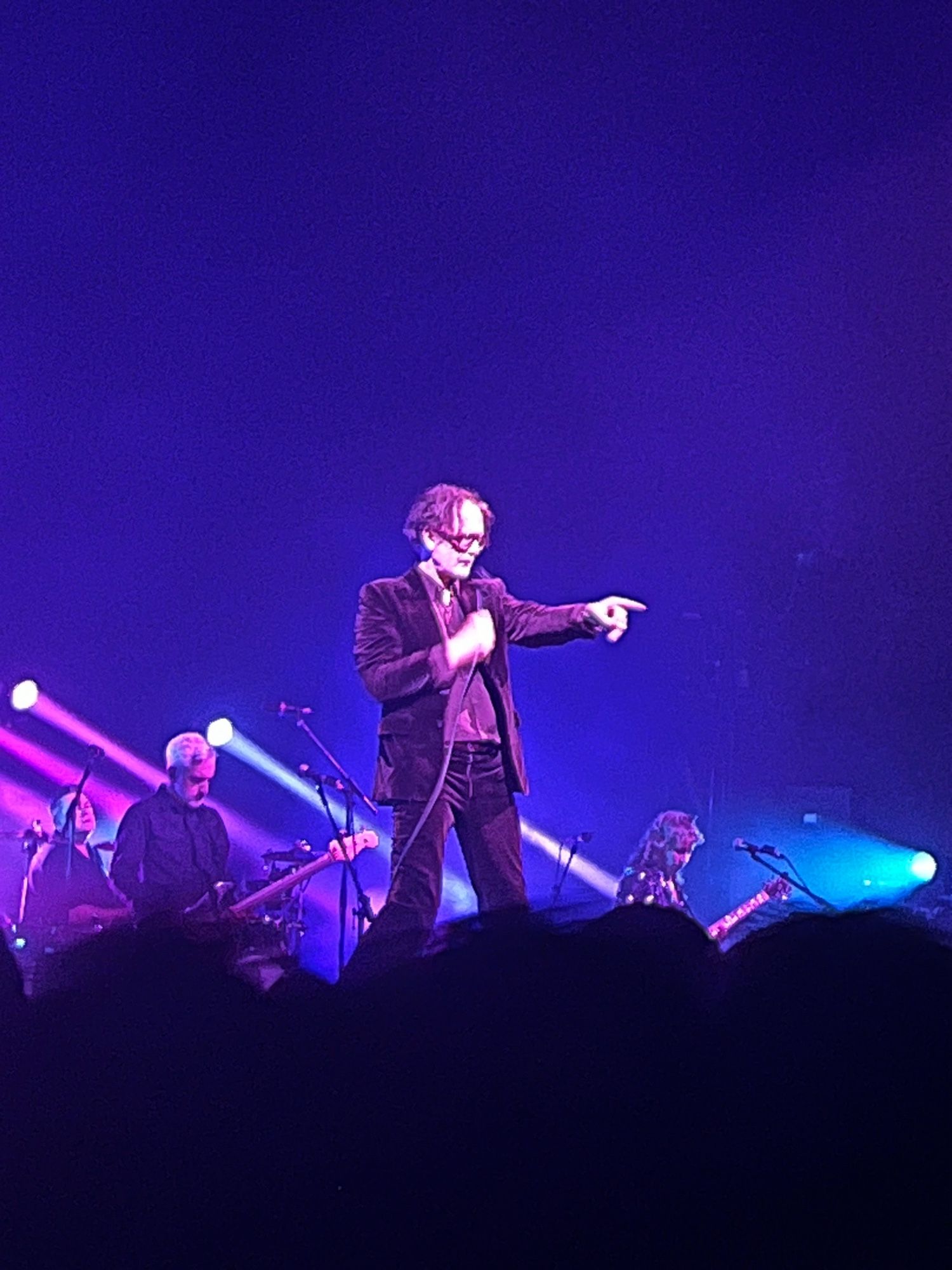 Jarvis Cocker of Pulp performs at Kings Theatre. He’s wearing a brown suit and is set against a blue background.