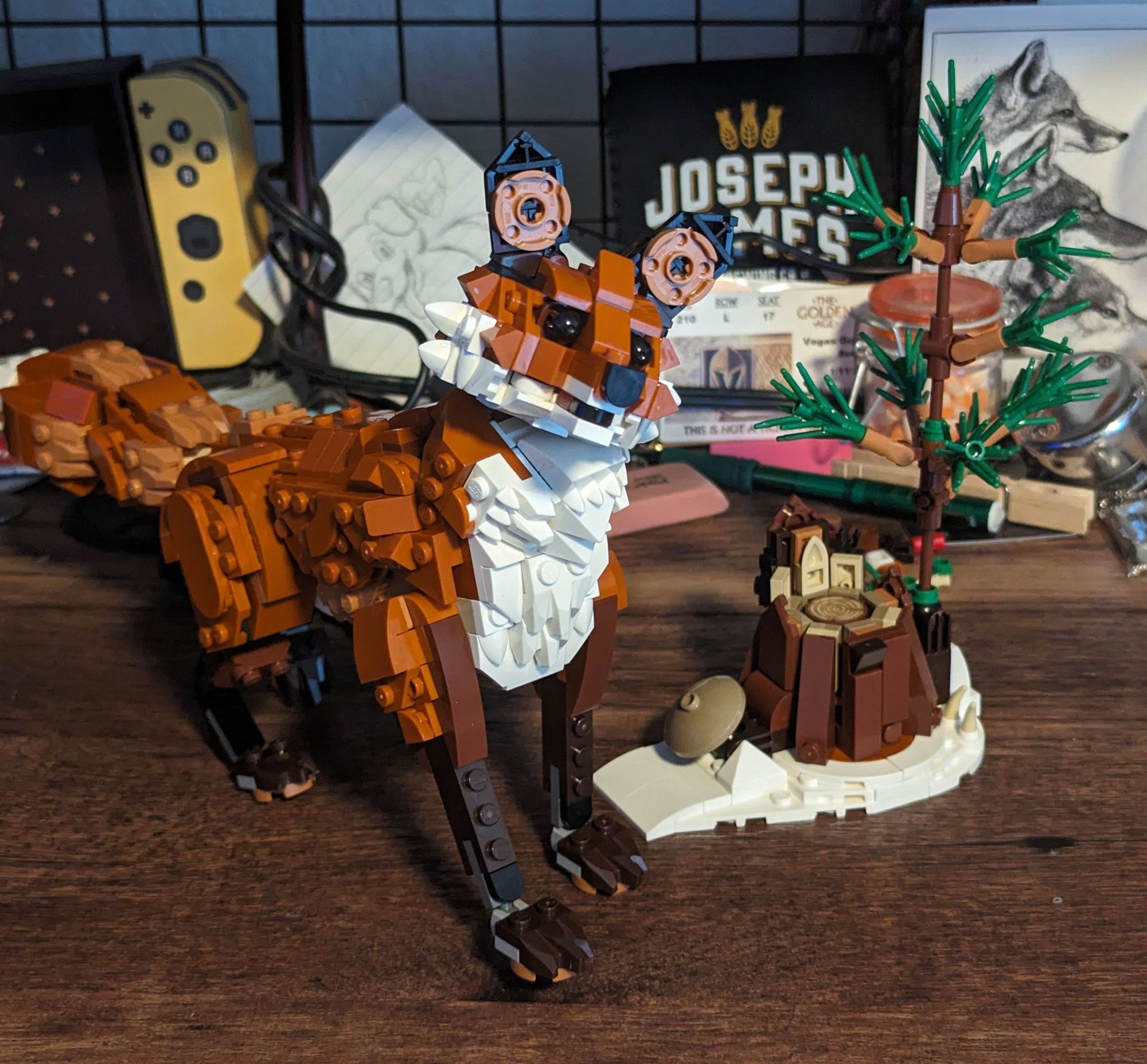 A, single, Lego branded fox standing upright and tilting its head. It stands beside a Lego tree stump, sprouting a single pine sapling. Both figures rest upon a messy desk; papers and knick-nacks haphazardly strewn about. The foxes face exudes curiosity for an off camera point, stopping in mid-step upon the sight.