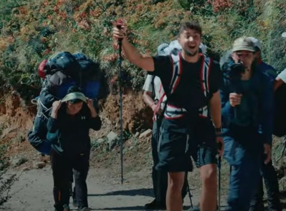 photo de son expédition, il est souriant entouré de photographes, et derrière un sherpa en souffrance porte un sac à dos plus gros que lui