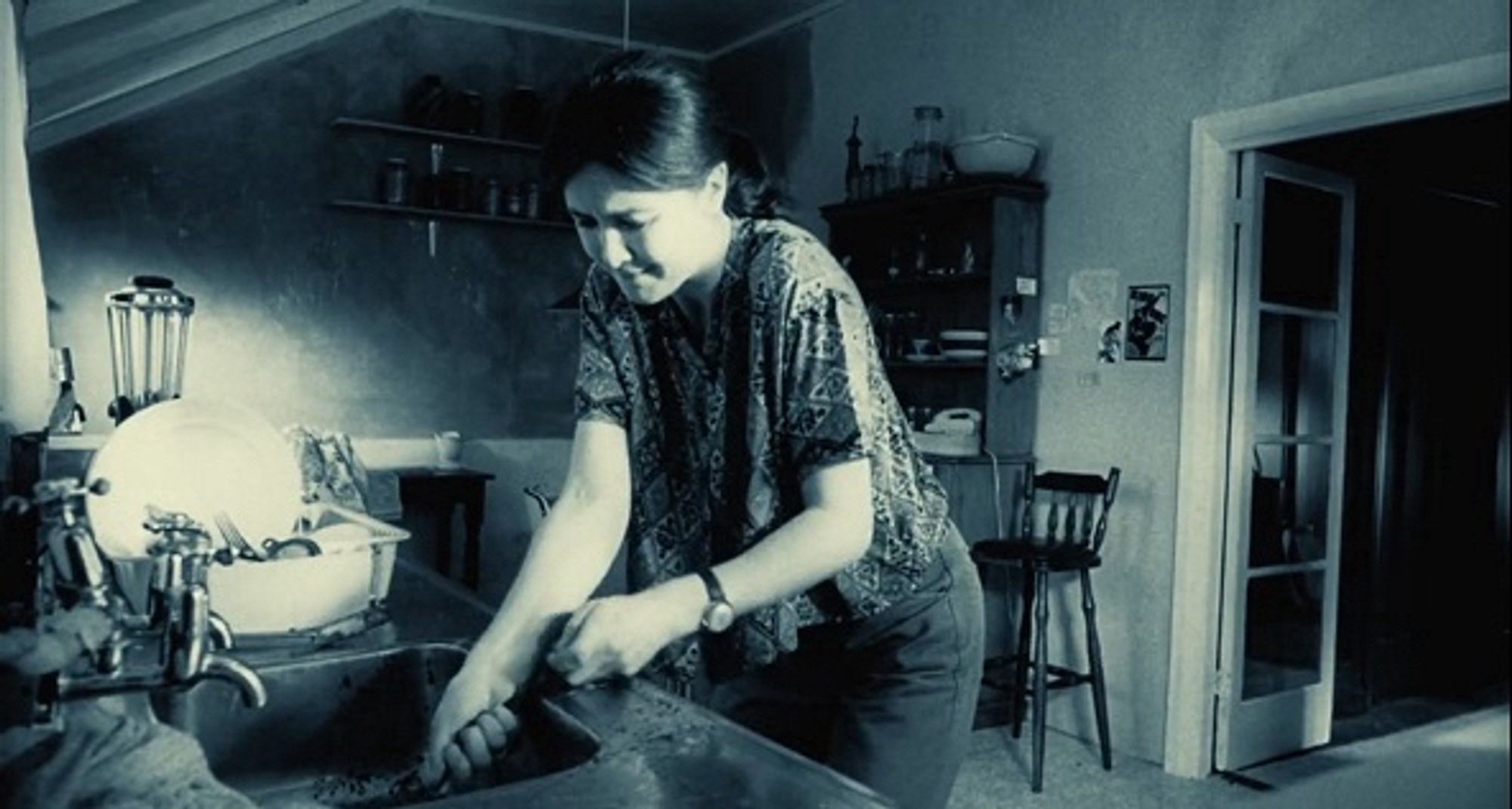 A woman pulls a very long clump of hair out of her kitchen sink.