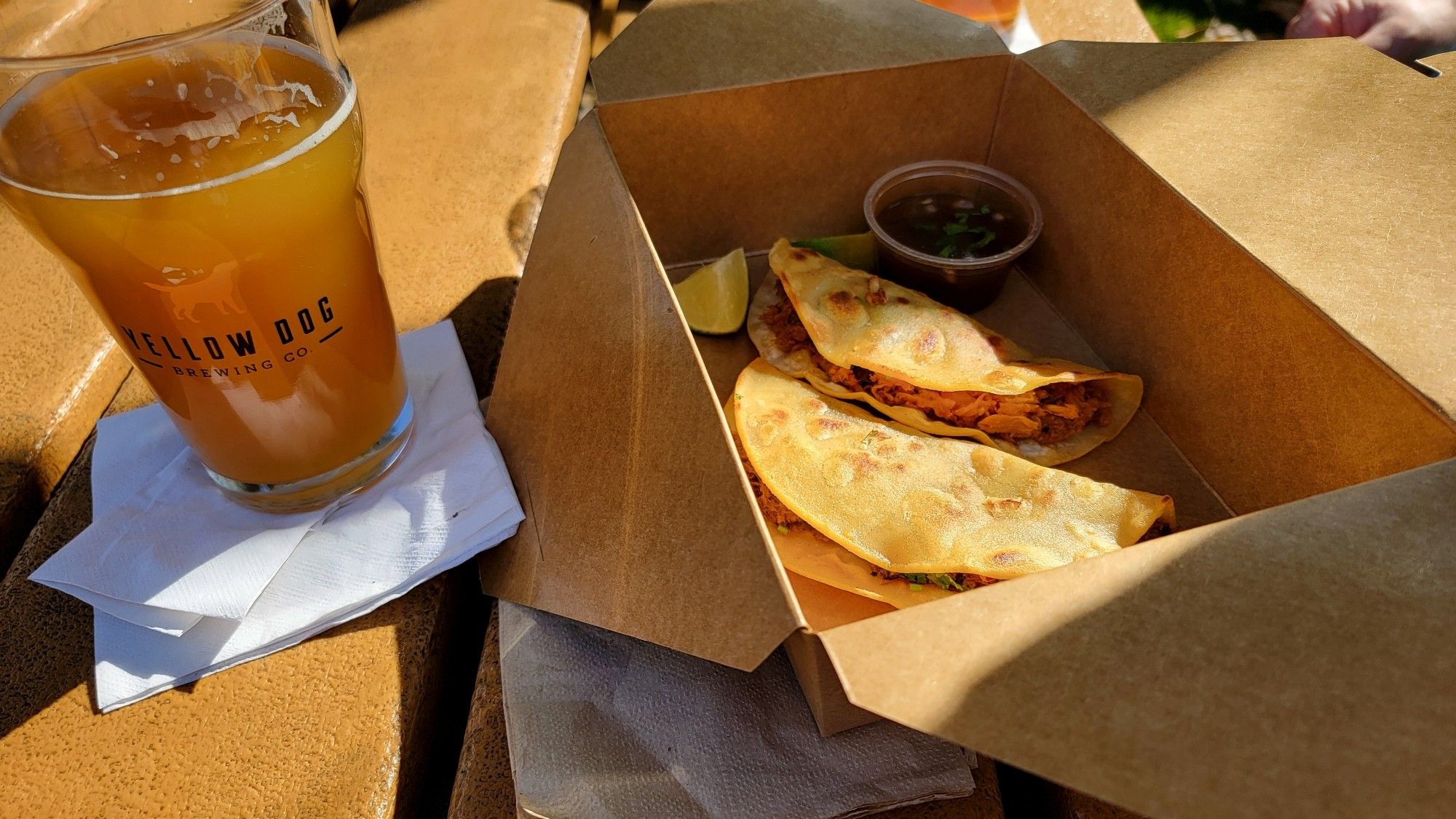 Glass of beer and two tacos in a box on a sunny table