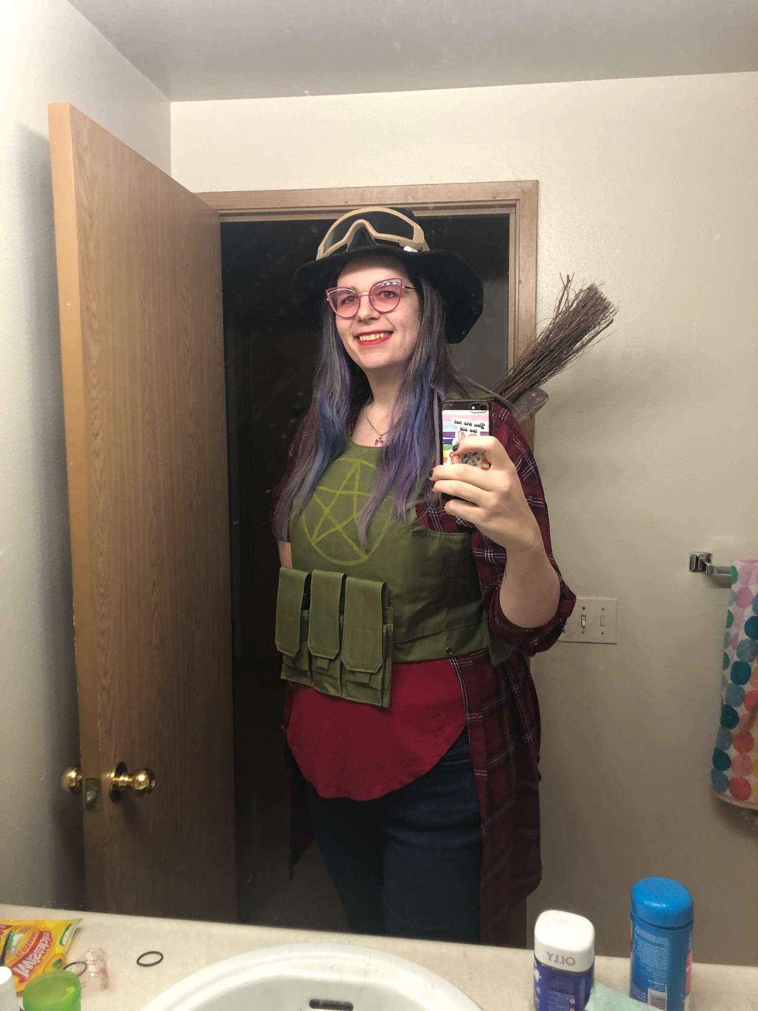 Bathroom mirror selfie with a partially-constructed Jen Kellen costume: witch hat with aviator goggles around the brim, tactical vest with pentagram insignia and a broom attached to the back.