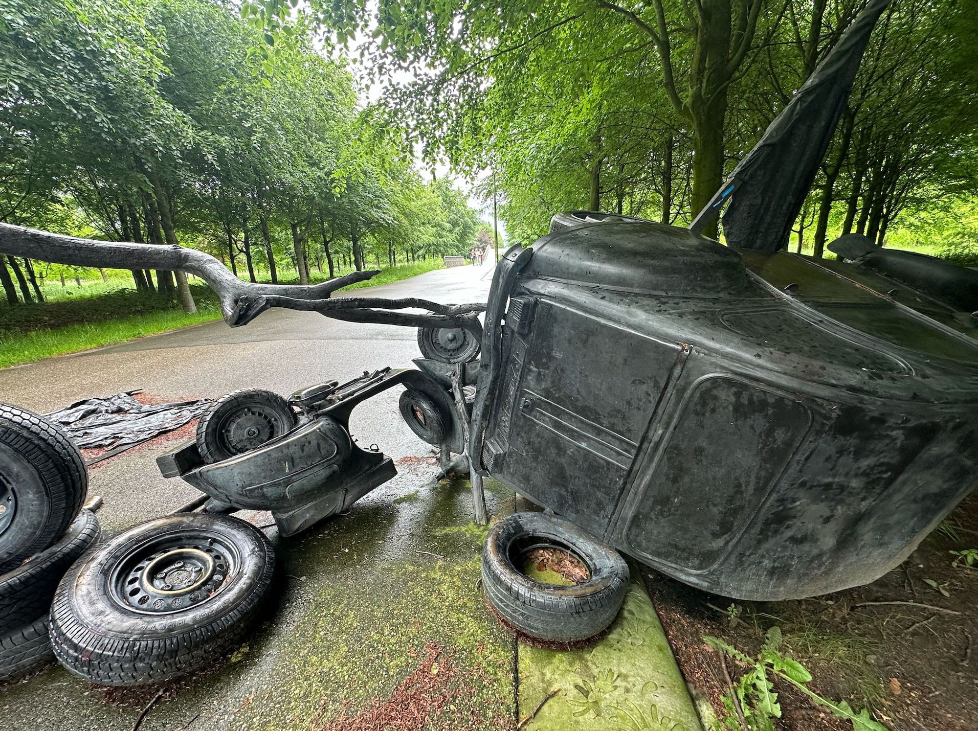 Barricade (2009) by Fernando Sánchez Castillo in Maximapark, Utrecht with bronze Vespa, tires, Citroen and Fiat in the foreground, trees in the background.