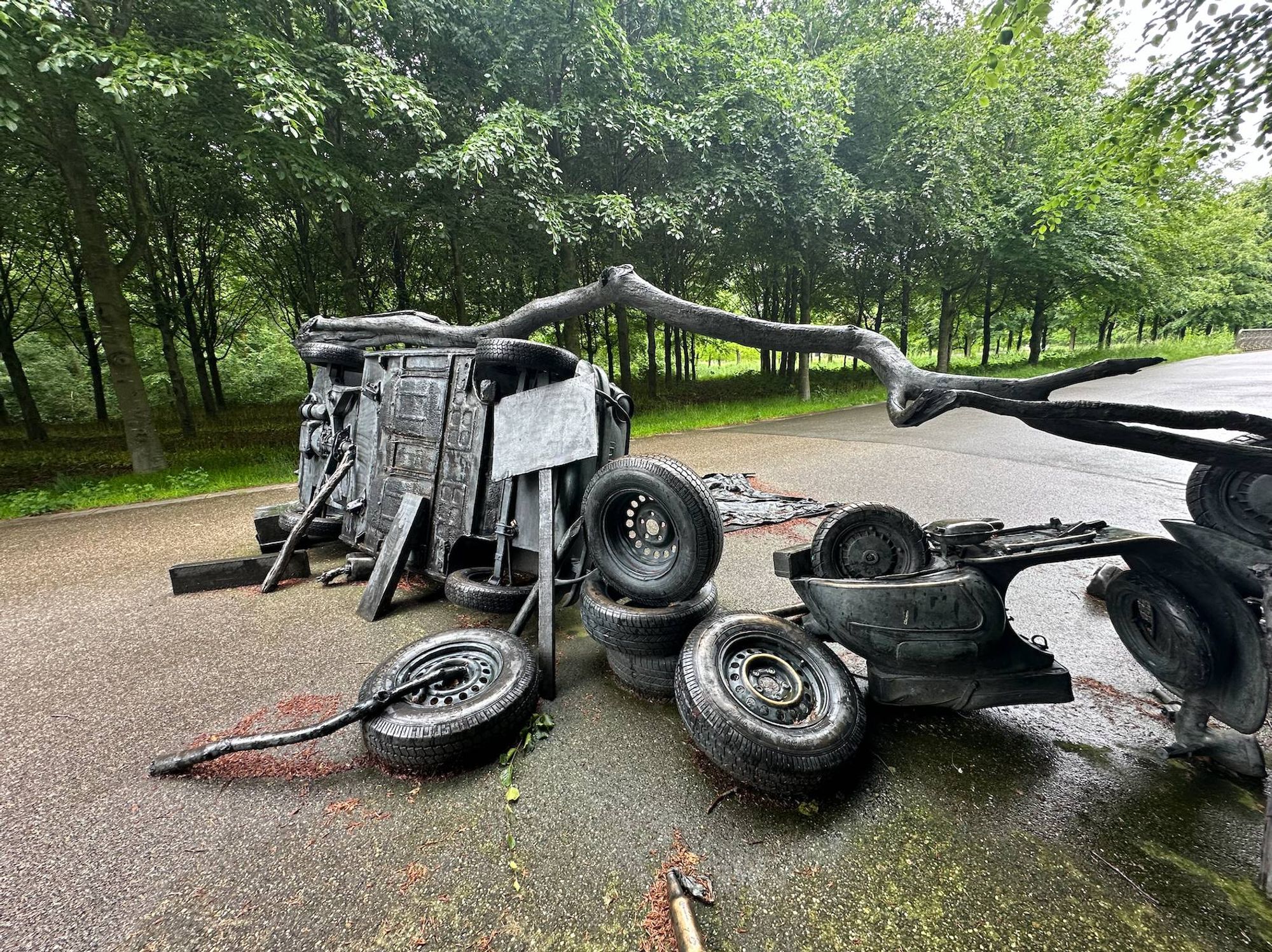 Barricade (2009) by Fernando Sánchez Castillo in Maximapark, Utrecht with bronze Vespa, tires, Citroen and Fiat in the foreground, trees in the background.