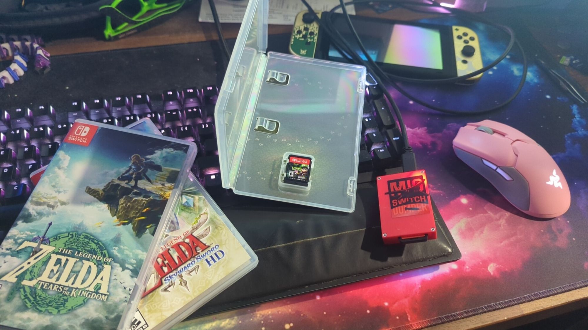 A photo showijg the MigSwitch Dumper with a game inside being dumped to my PC. There are 3 game cases in the frame for, Zelda Tears of the Kingdom, Zelda Skyward Sword, and Luigi's Mansion Dark Moon (2) HD. Also in the frame is my Nintendo Switch console