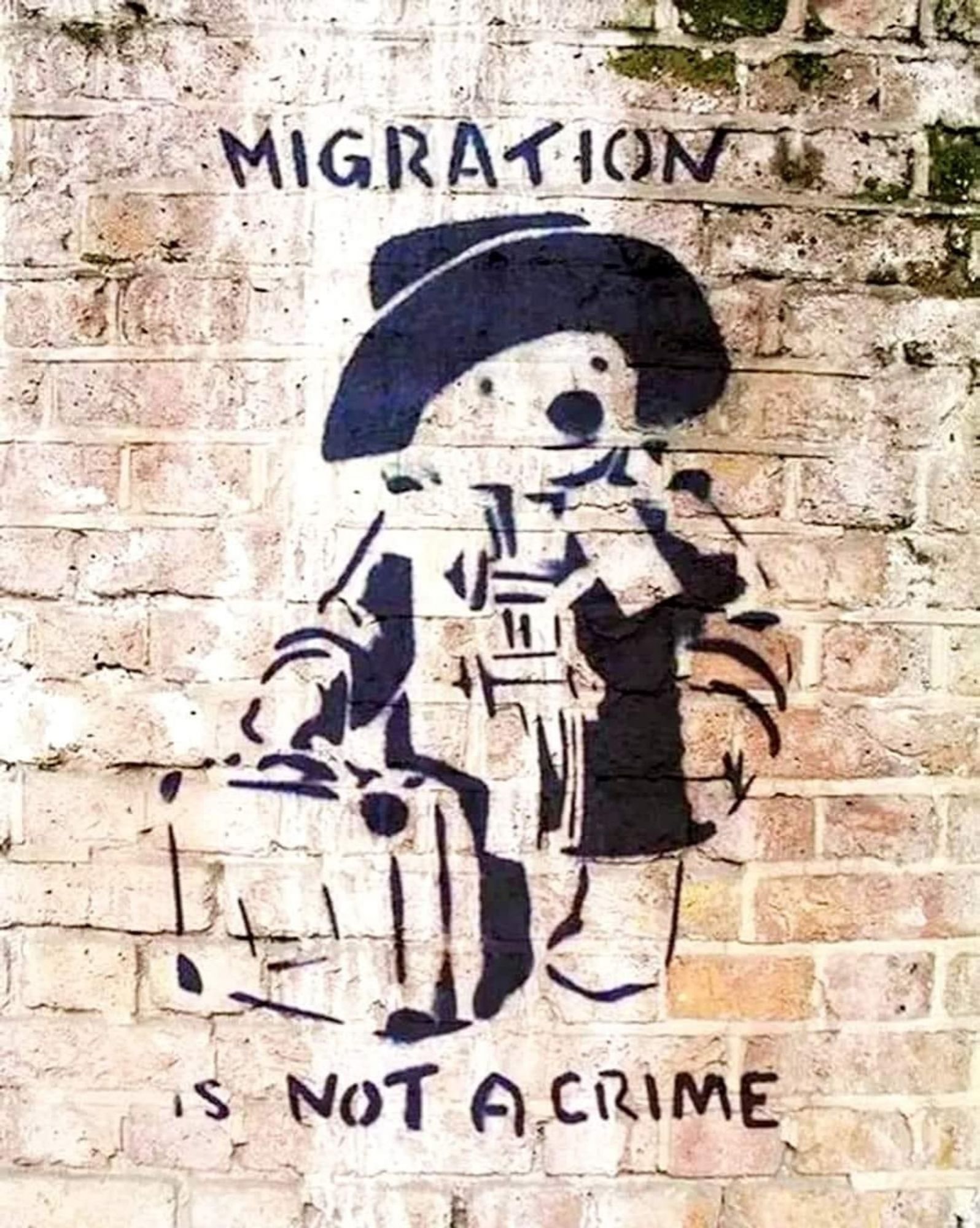 Ein Graffiti von Banksy
Ein Teddybär, gekleidet mit Mantel und Hut. Er trägt einen Koffer und eine große Tasche. Über ihm steht "Migration", unter ihm: not A crime