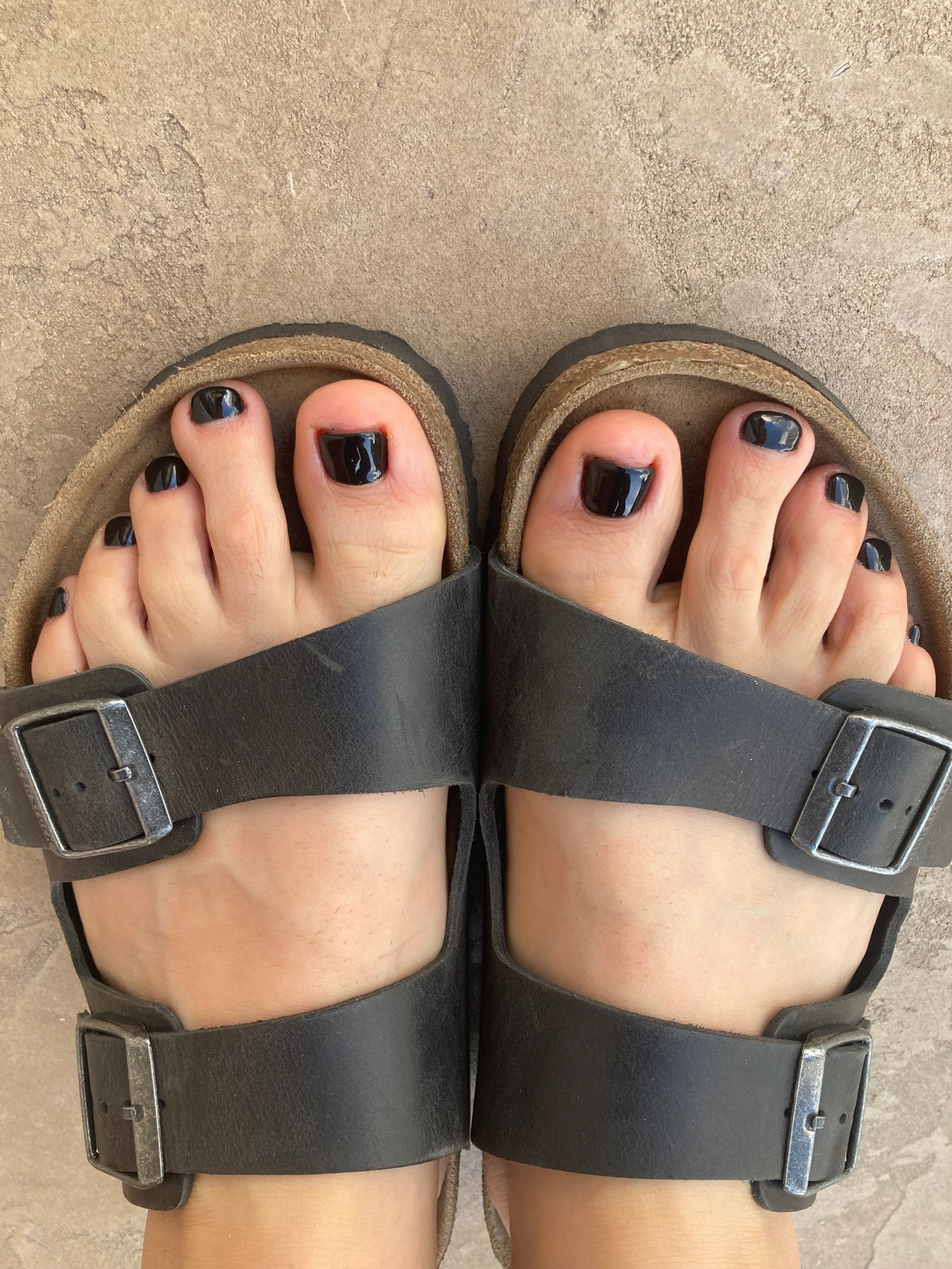 Two bare feet in Birkenstocks. The toenails have fresh new black gel polish.