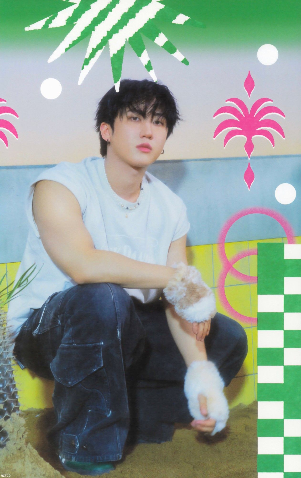 Changbin is dressed in a white t-shirt and dark jeans, and white plush gloves. He is crouched inside an empty pool with sand and yellow tiles. 