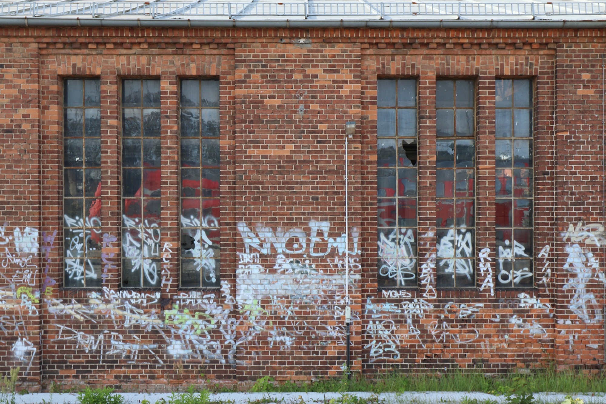 An abandoned train house, red brick, white graffiti reached halfway up. In the large windows a reflection of a Regiobahn train.