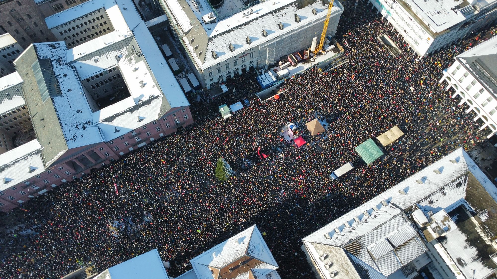 Der Marktplatz in Karlsruhe von oben. Er ist voller Menschen, die sich bis in die angrenzenden Seitenstraßen verteilen.