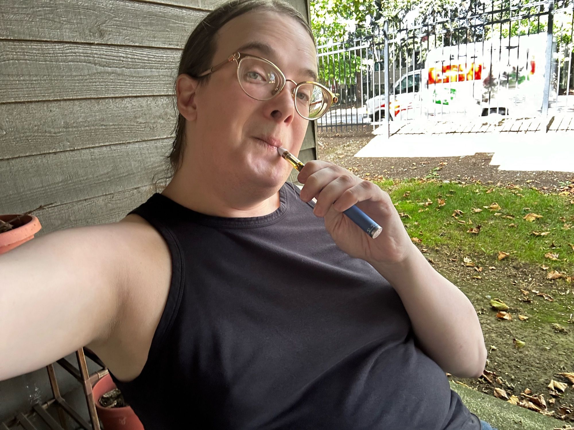 Karie on her patio in a black tanktop with her hair pulled back. She’s vaping weed.