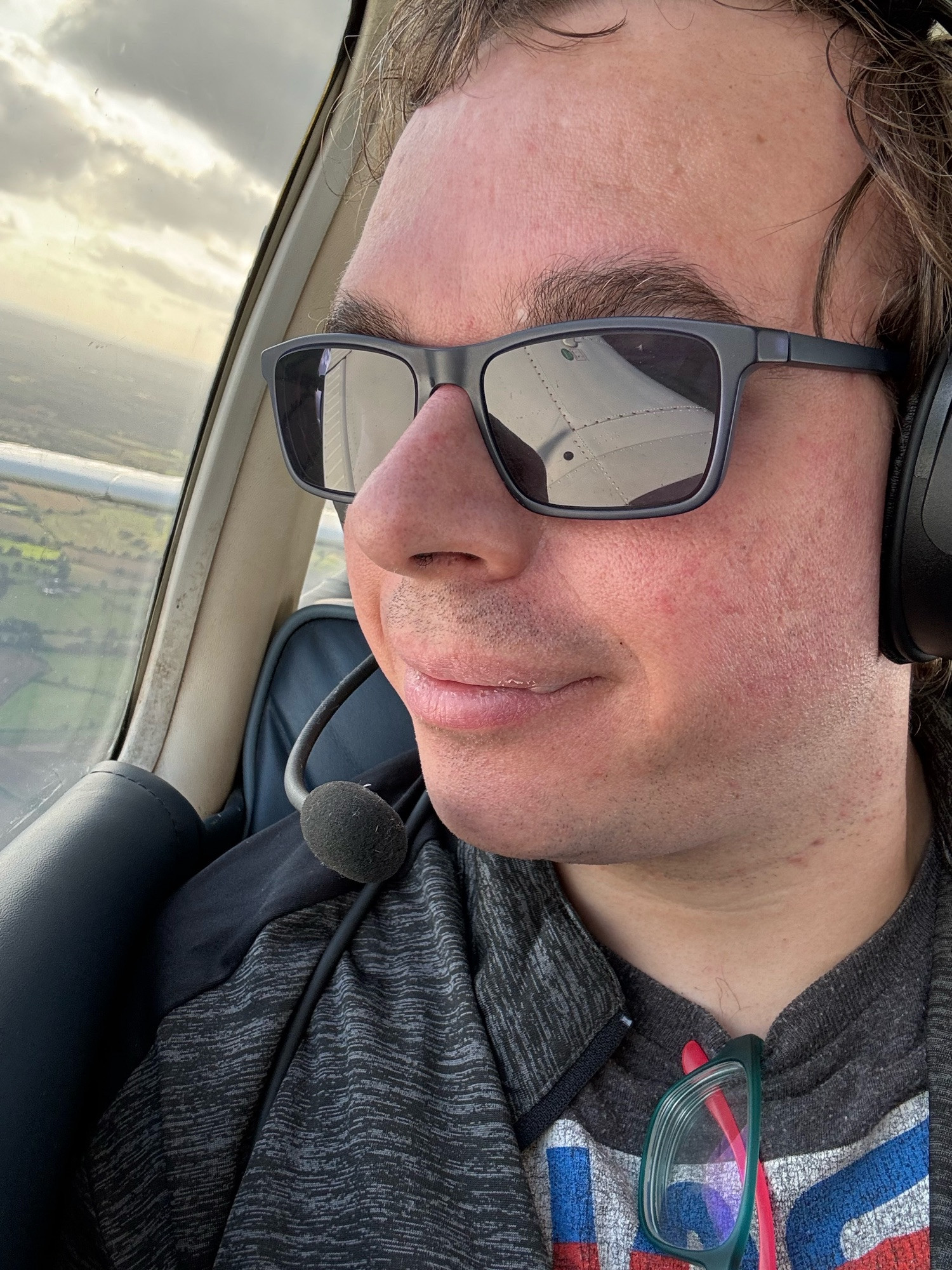 Jamie looking out the window of a light aircraft, wing and sky reflected in his glasses.