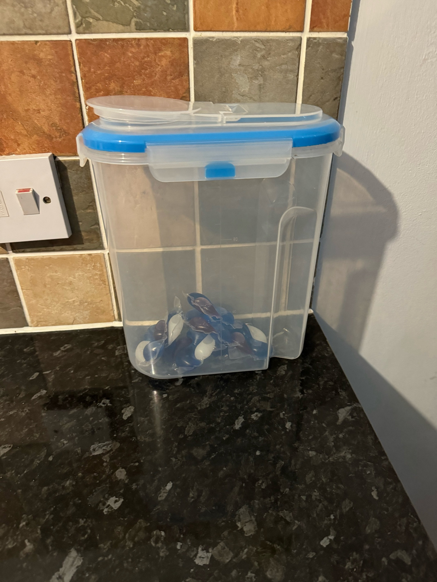 A photo of a tub on Jamie’s kitchen worktop. It’s the type used for holding cereal except it is full of the washing tabs used for laundry. It had an easy access flip open top.