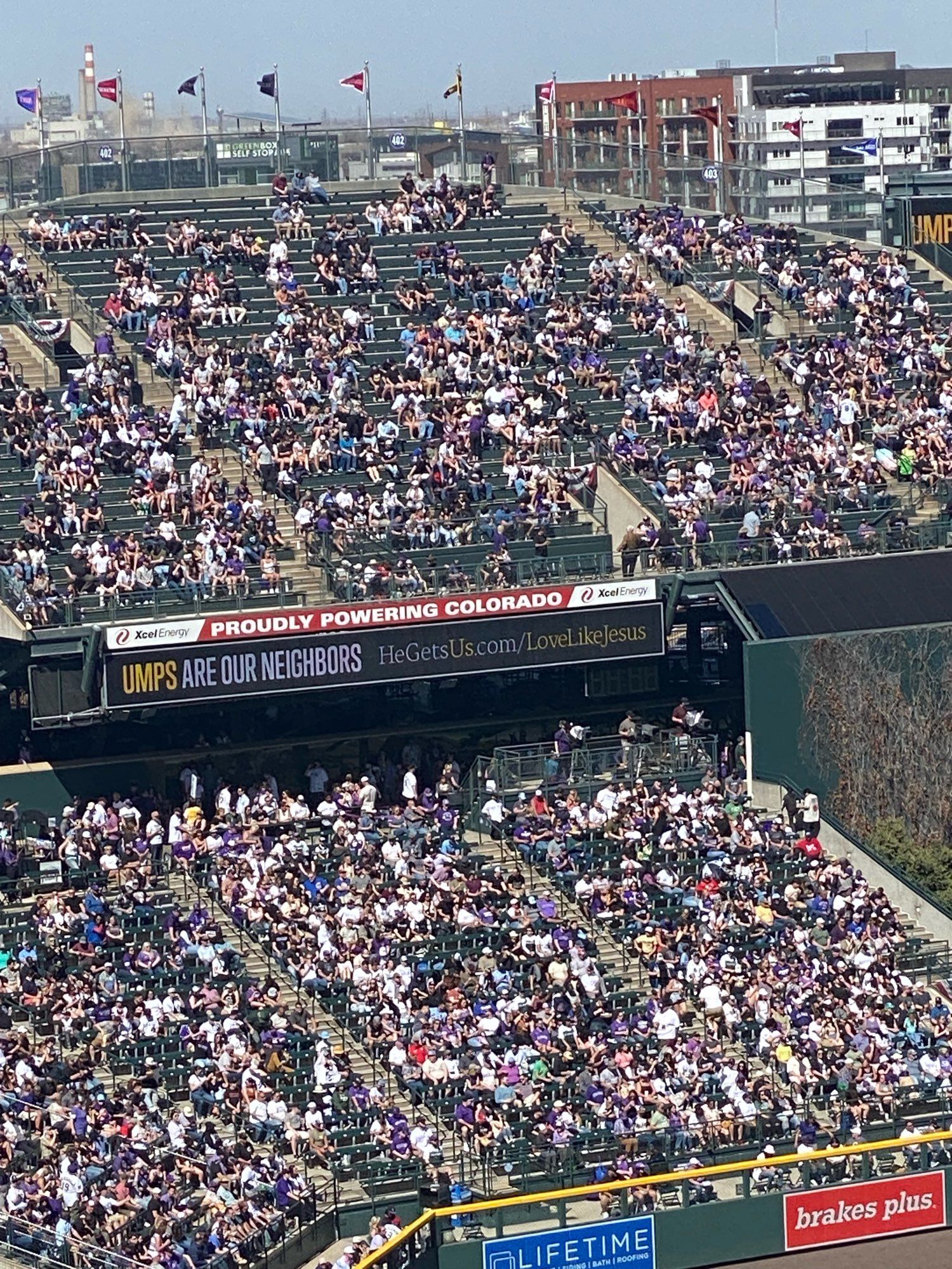 Photo of packed stands at a ball park. A video sign reads: “Umps are our neighbors. HeGetsUs.com/LoveLikeJesus”