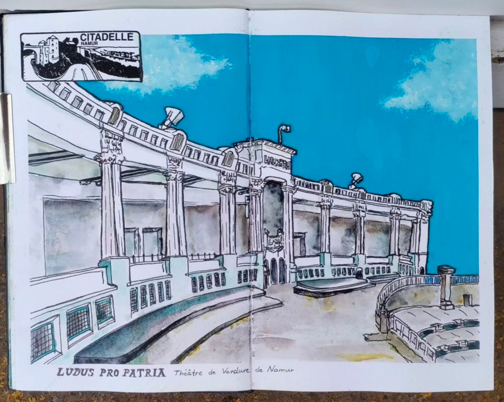 A doublepage in a sketchbook with a dynamic angle of the outdoor theatre in Namur, Belgium with a blue sky, done in ink, watercolor and guache