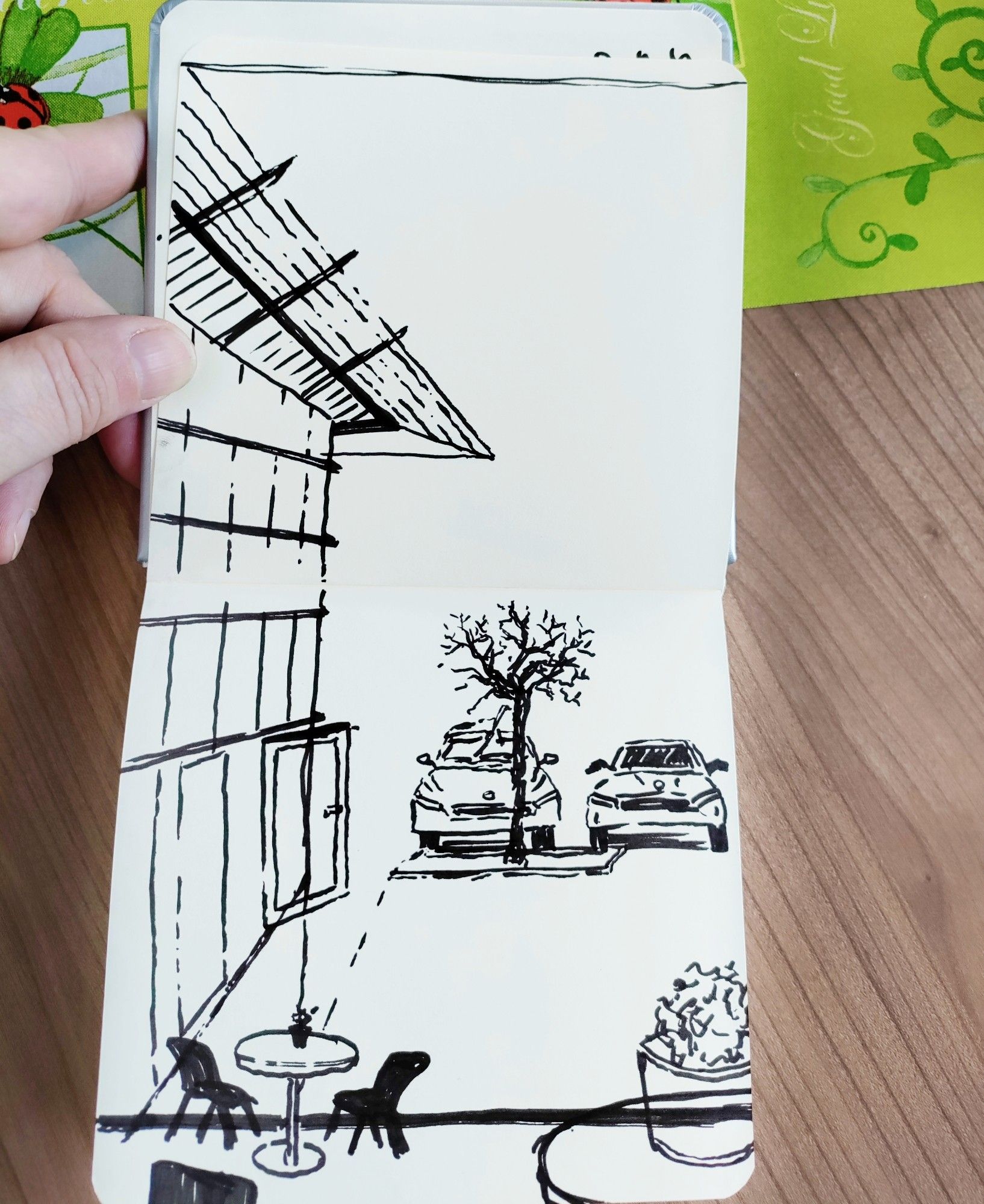 A sketchbook held open with the view sketched from a car dealership waiting area through the windows