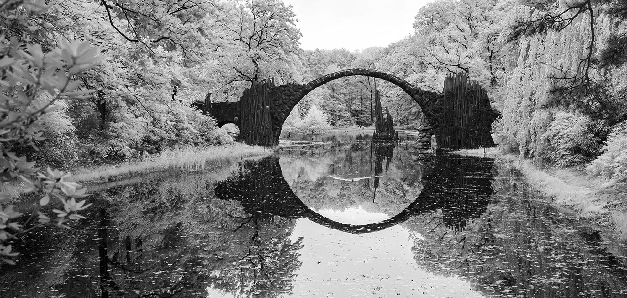 Infrared black and white image of the Rakotz Bridge in the park of Kromlau. Due to the infrared effect, all green leafs appear white.