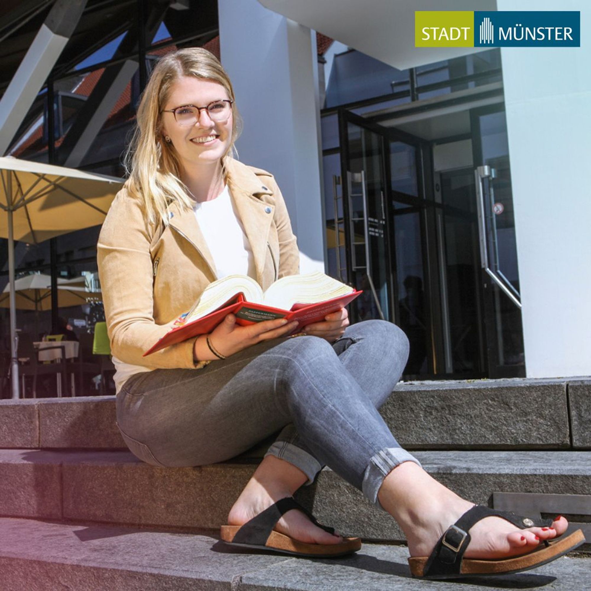 Junge Frau sitzt auf Treppenstufen und hält ein Buch in der Hand