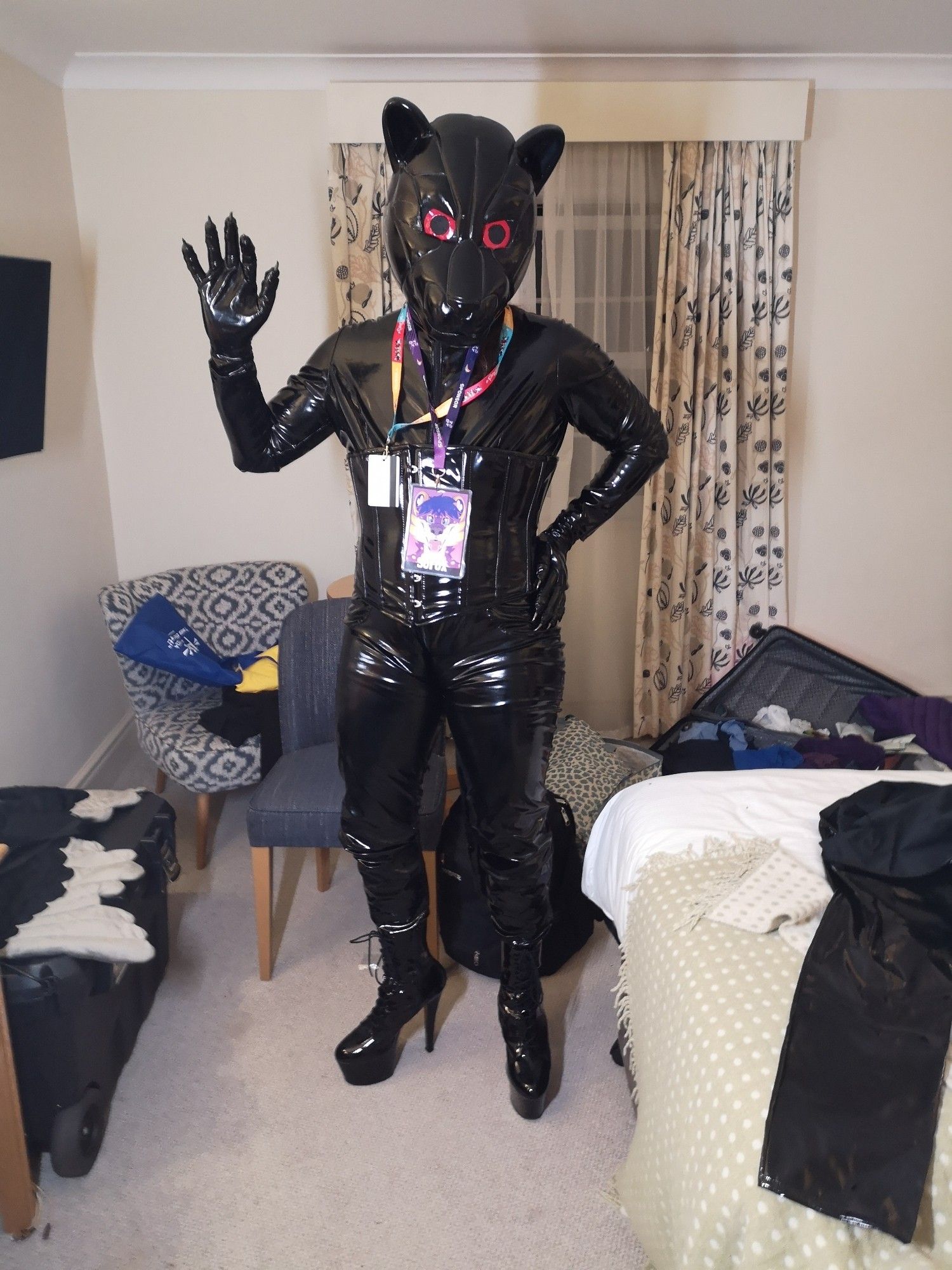 Sofox wearing a black shiny outfit with corset, heels and clawed gloves. The head is a helmet styled after a robotic jaguar with red eyes.